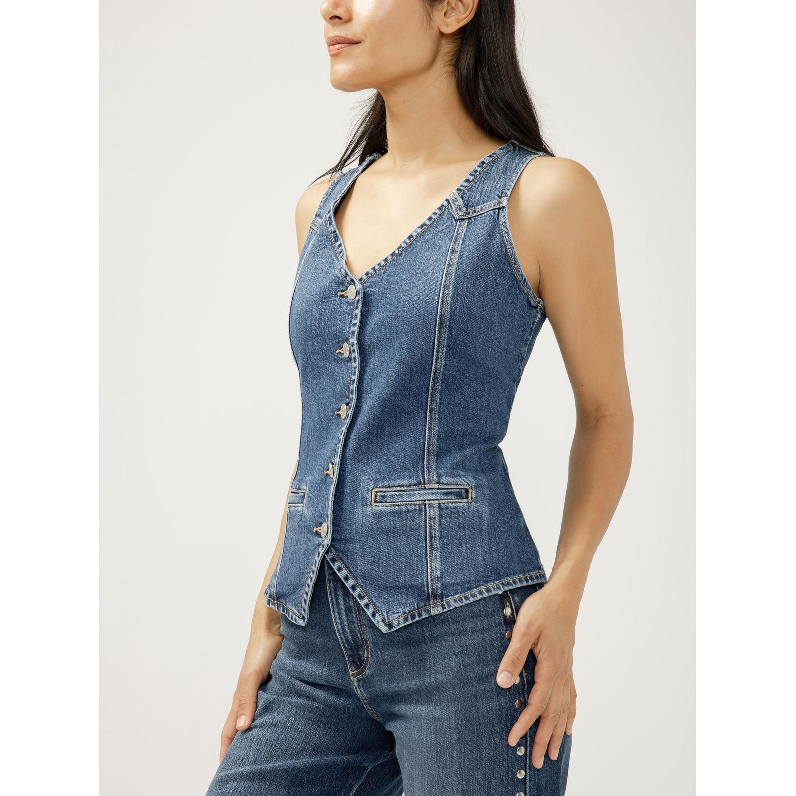 Model wearing blue denim longline vest with V-neck, button-front, welt pockets and pointed hem.