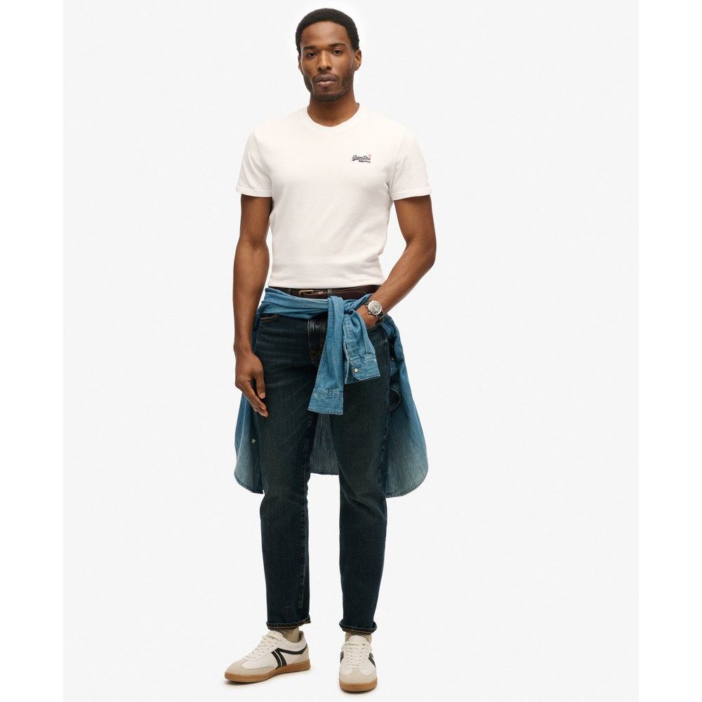 Model wears white Superdry Essential Embroidered Tee with chest logo, dark jeans, and a denim shirt tied at the waist.
