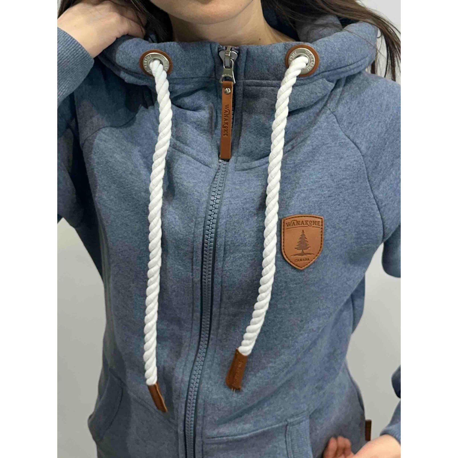 Wanakome Hera zip-front hoodie in blue terry fleece with white rope drawstrings, leather caps, and chest patch logo.
