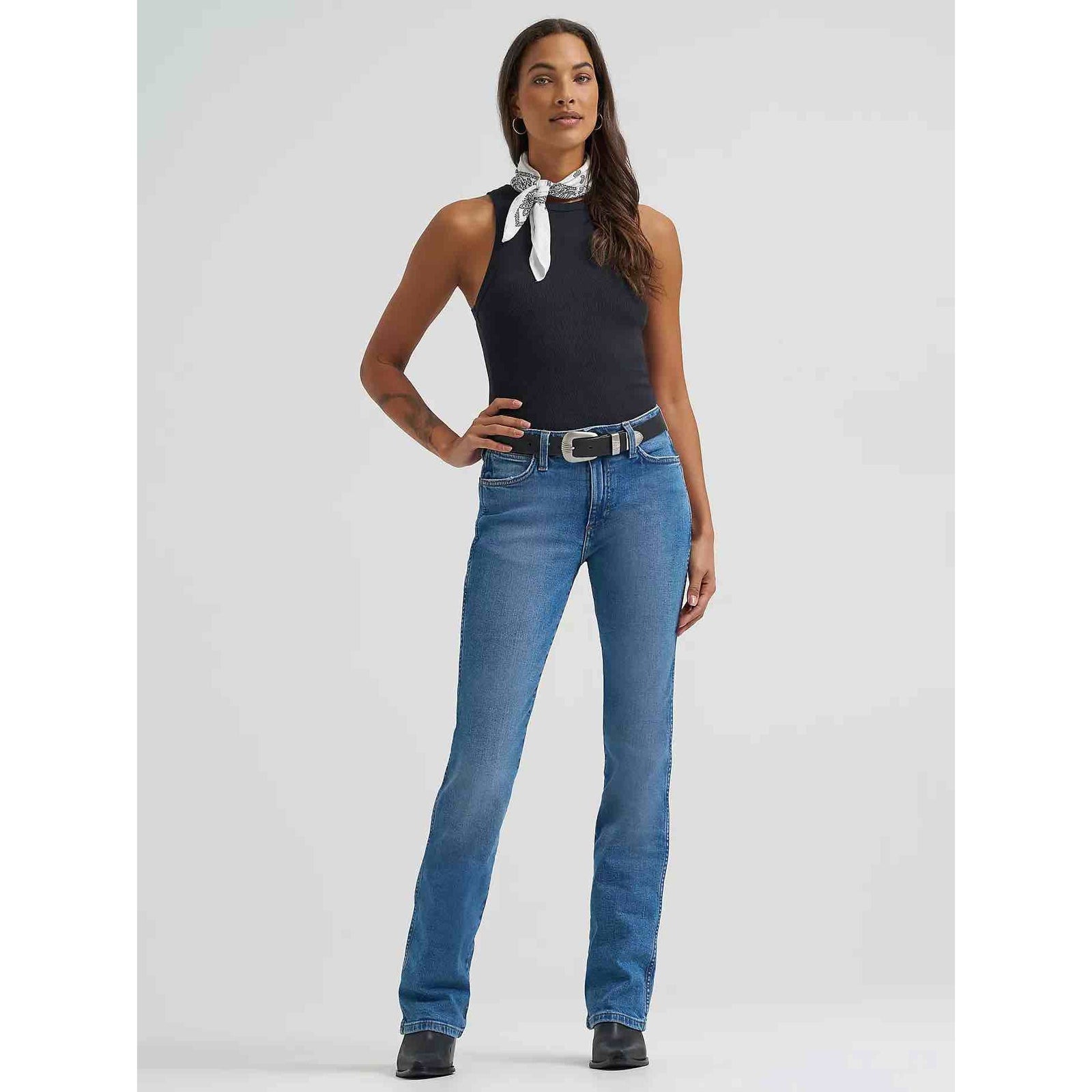 Model wearing Women's Wrangler Retro Bailey High Rise Bootcut Jean in blue wash with belt.