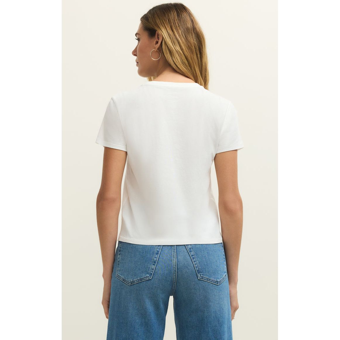 Back view of a model wearing a white Z Supply Dolce Tourist Tee with blue jeans.