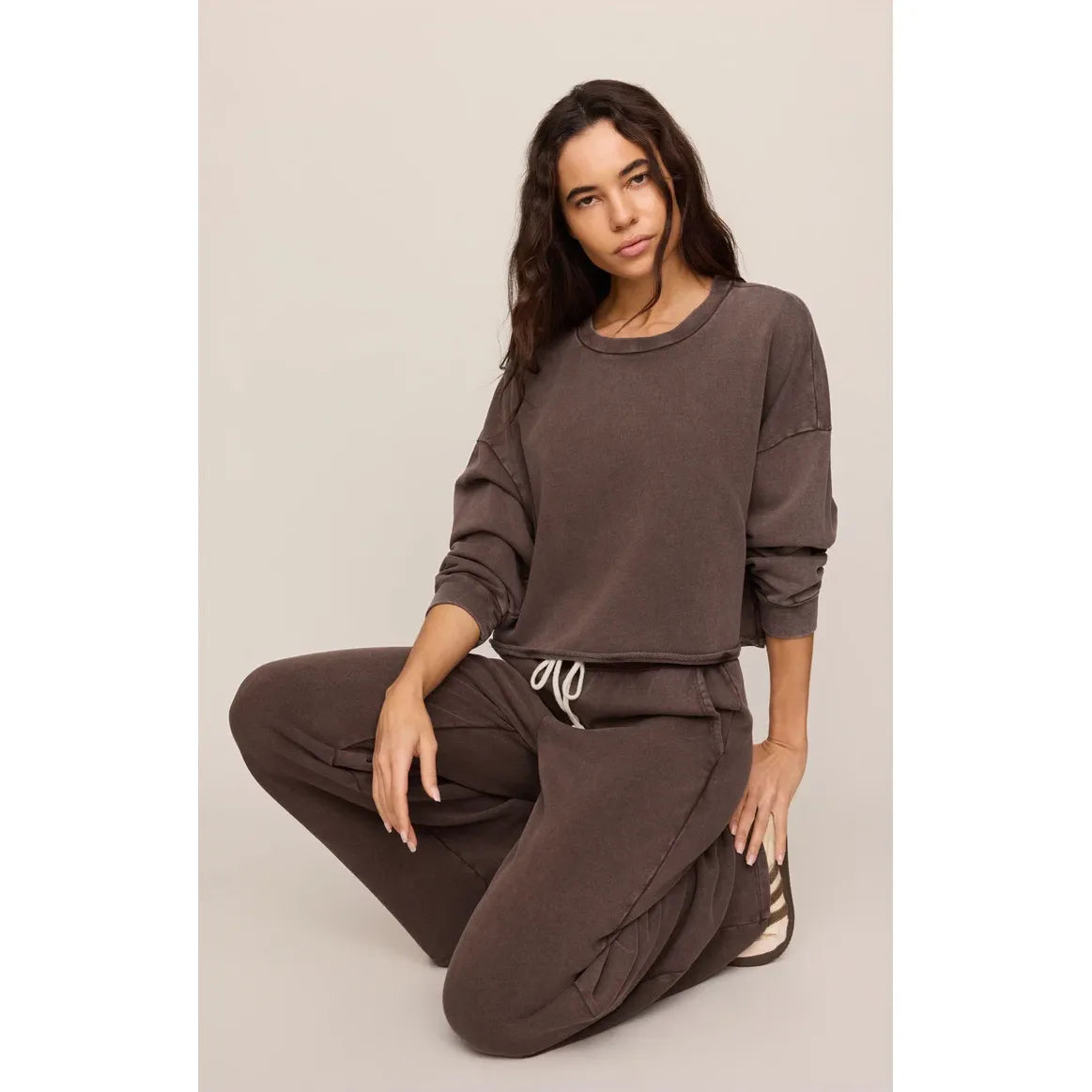 Model crouching in brown Z Supply Hunter Knit Pants with white drawstring and large slash pockets, crafted from soft cotton French terry for relaxed comfort.