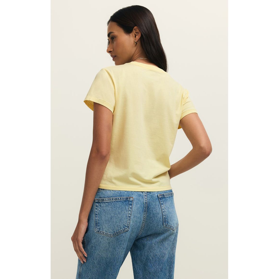 Back view of a woman in a pale yellow Z Supply Shine Tourist Tee with a relaxed fit and blue jeans.