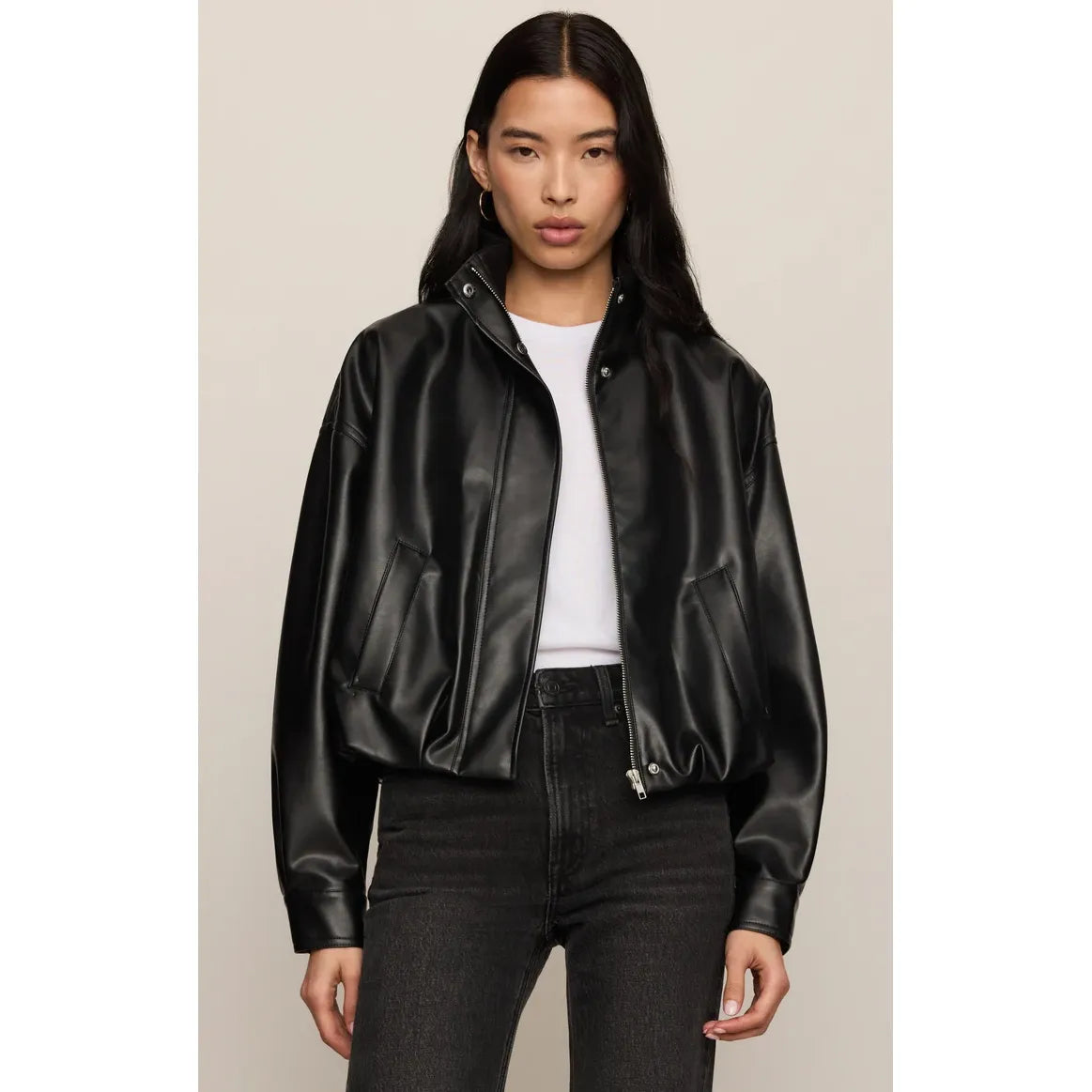 Black faux leather bubble jacket with funnel neck, hidden zip, and voluminous gathered hem worn over white top.