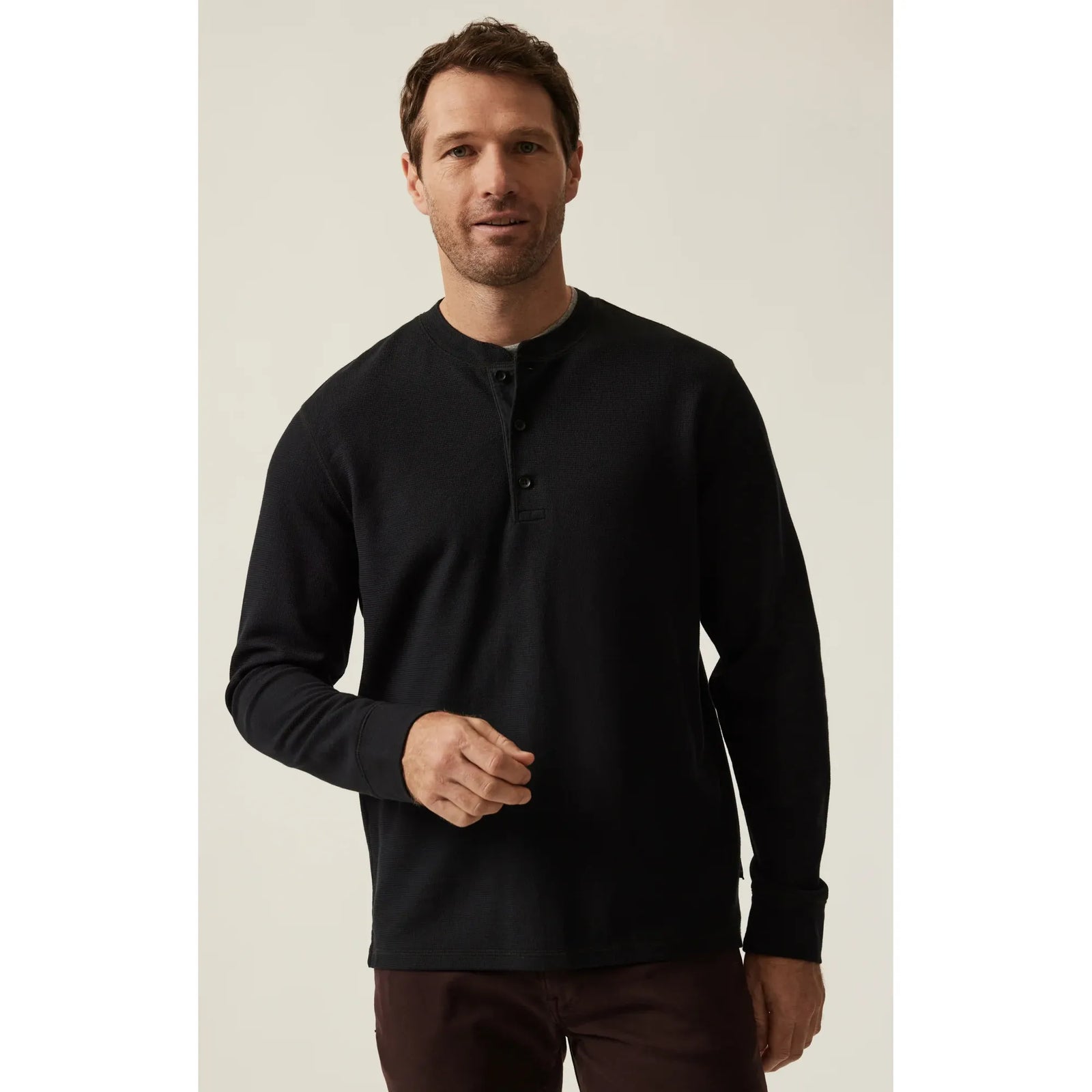 Man wearing black 34 Heritage Long Sleeve Henley with button placket, seated.