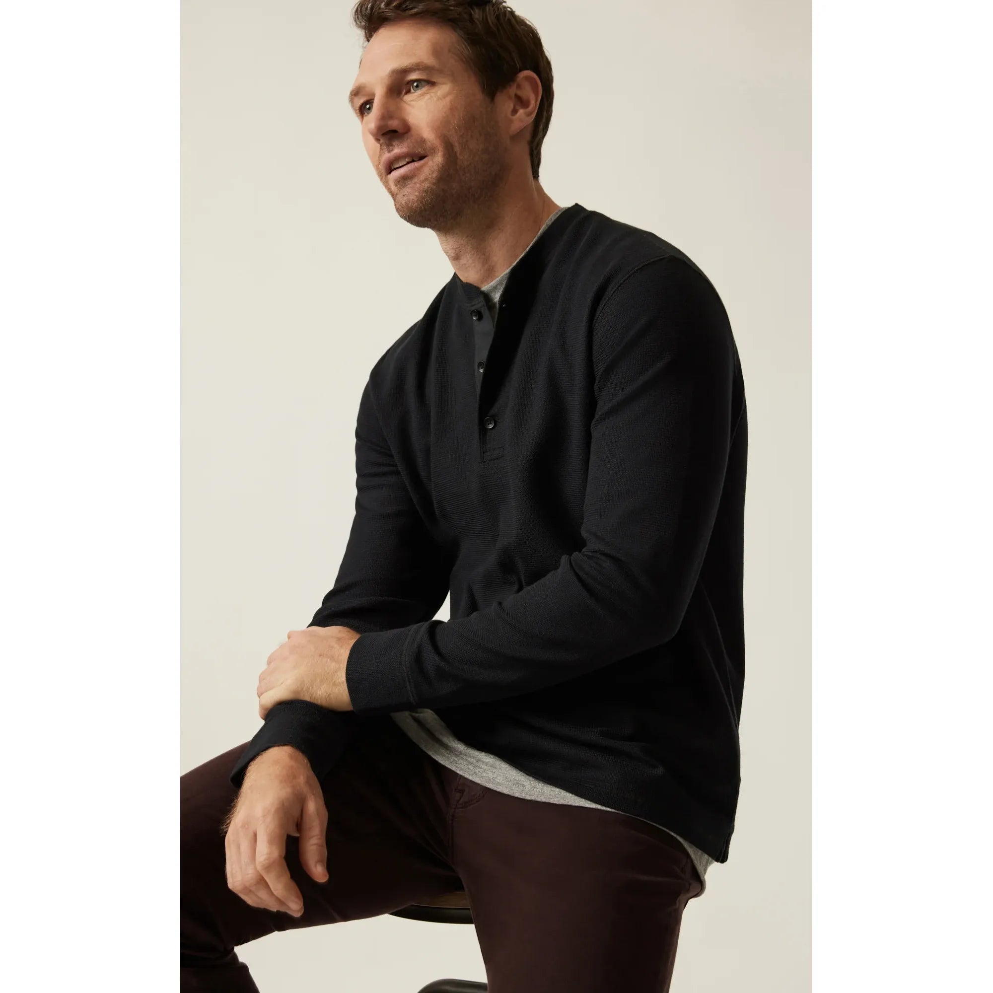 Man wearing black 34 Heritage Long Sleeve Henley with button placket, seated.