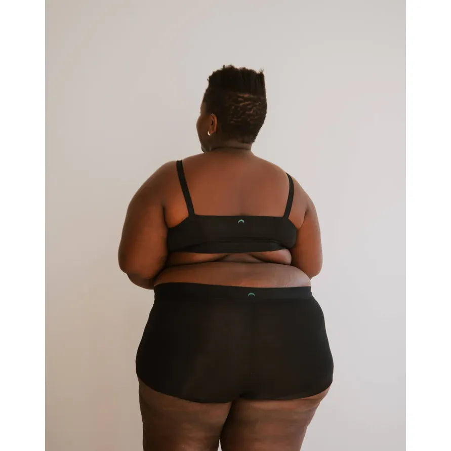 Huha Boxer Mineral Undies: back view of a plus-size person in black boxers with teal logo waistband and cuffless legs.