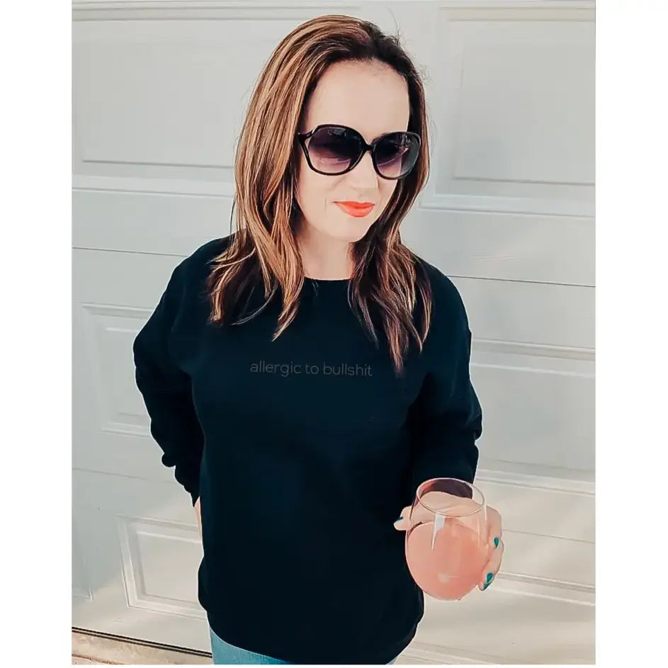 Stylish woman in the Allergic to Bullsh*t Crew sweater, holding a drink and showcasing a bold attitude.