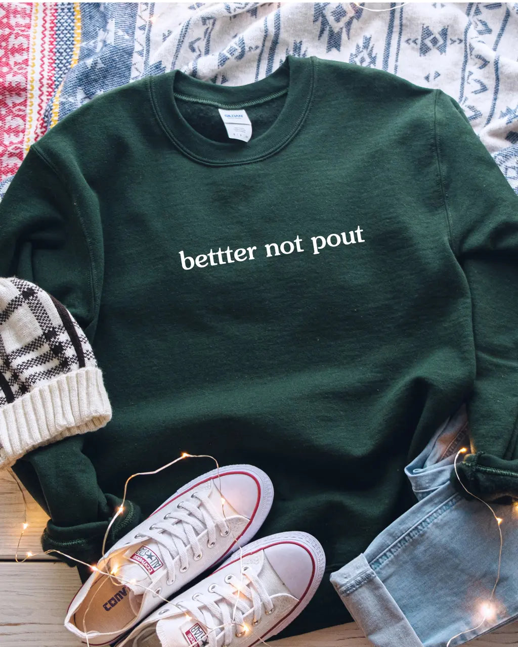 Forest green crewneck sweatshirt featuring "bettter not pout" in white lowercase text, styled with sneakers and holiday lights.