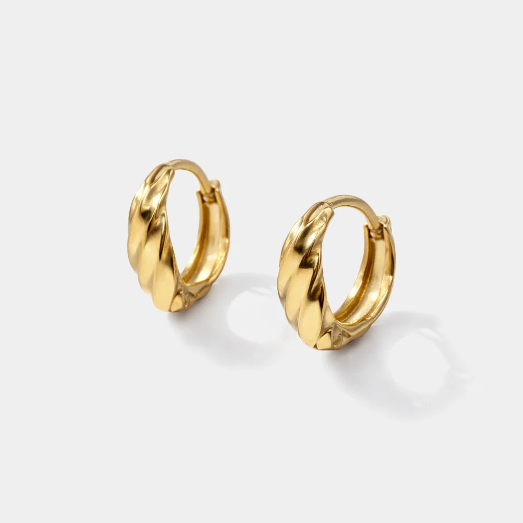 Wavy gold-tone hoop earrings with twisted texture that catches the light.