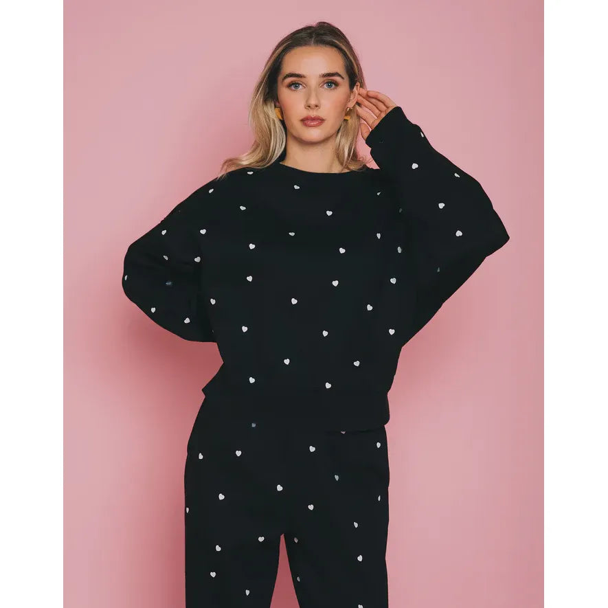 Model in Brunette the Label All Over Tiny Heart Crew black loungewear set with white tiny hearts.