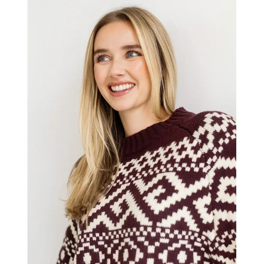 Blonde woman smiling in a deep plum Fair Isle knit sweater featuring a bold cream geometric pattern across the chest.
