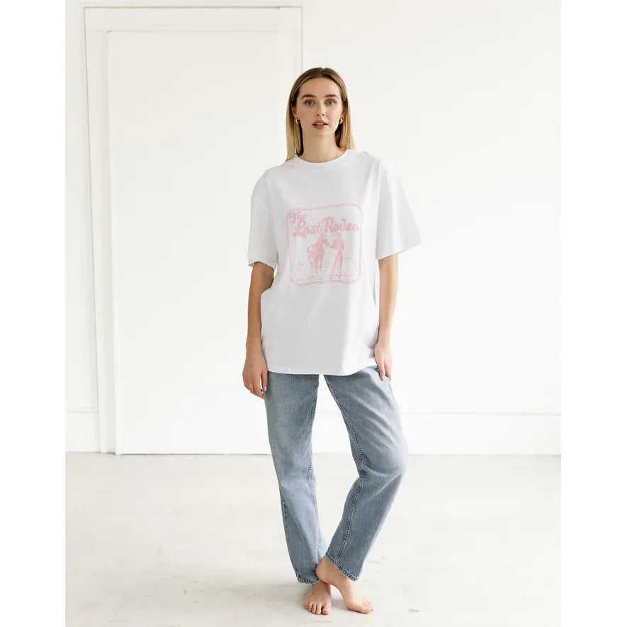 Model wearing Brunette the Label Last Rodeo Boxy Tee in white with pink graphic, oversized fit, barefoot in studio.