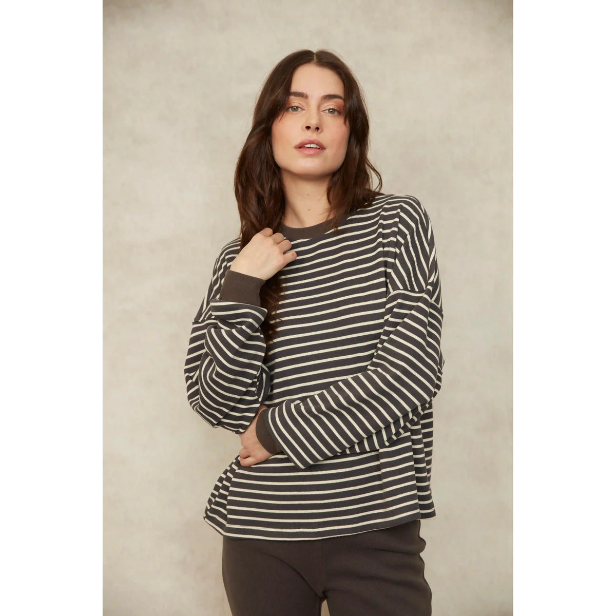 Model wearing a relaxed fit long sleeve striped waffle top with horizontal dark and light bands and ribbed cuffs.