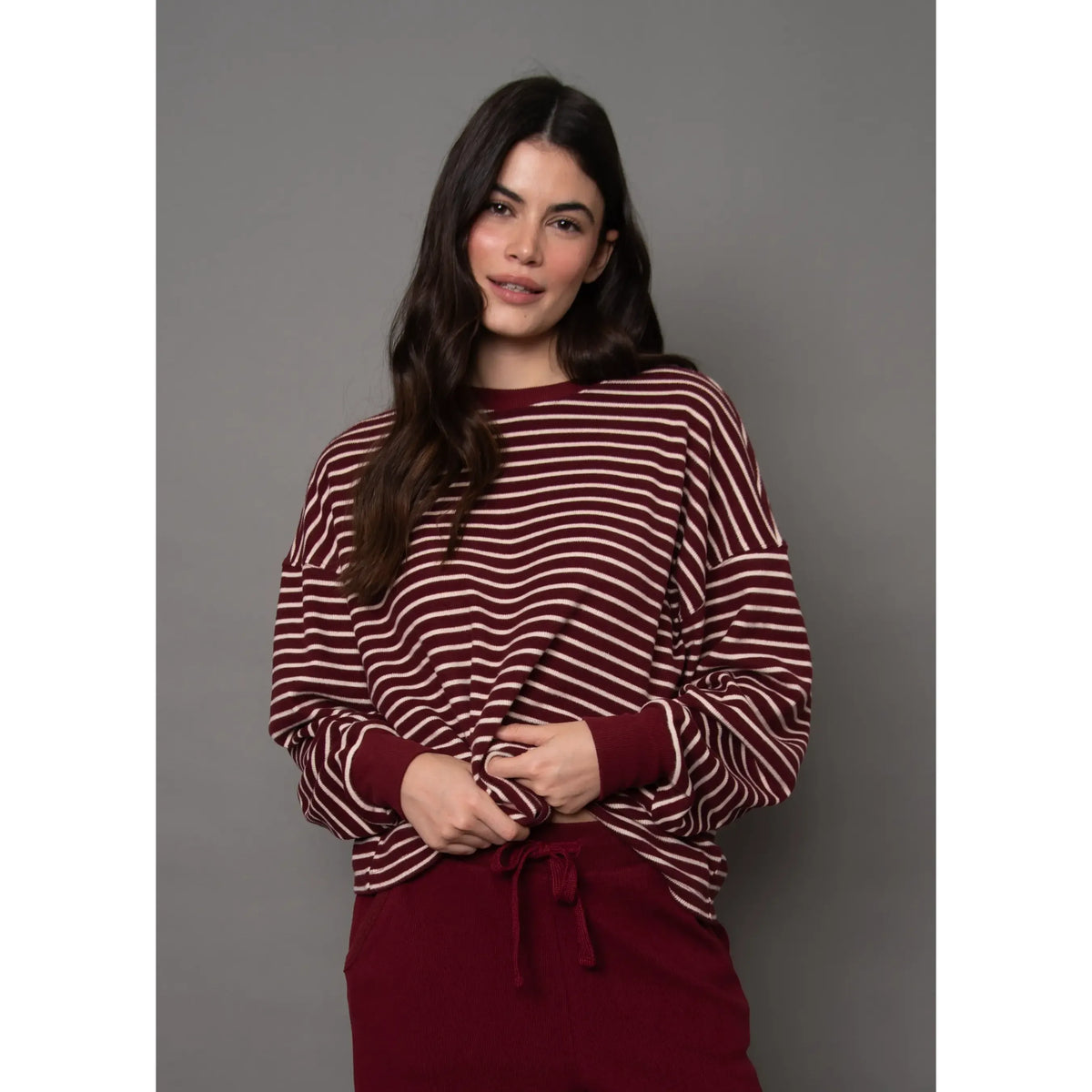 Model wearing burgundy and cream striped waffle knit top with relaxed fit long sleeves and horizontal stripe pattern.