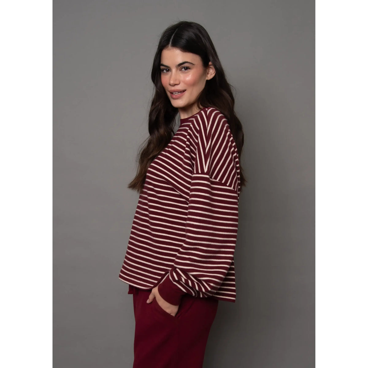 Model wearing a burgundy and white striped waffle knit top with long sleeves and relaxed fit.