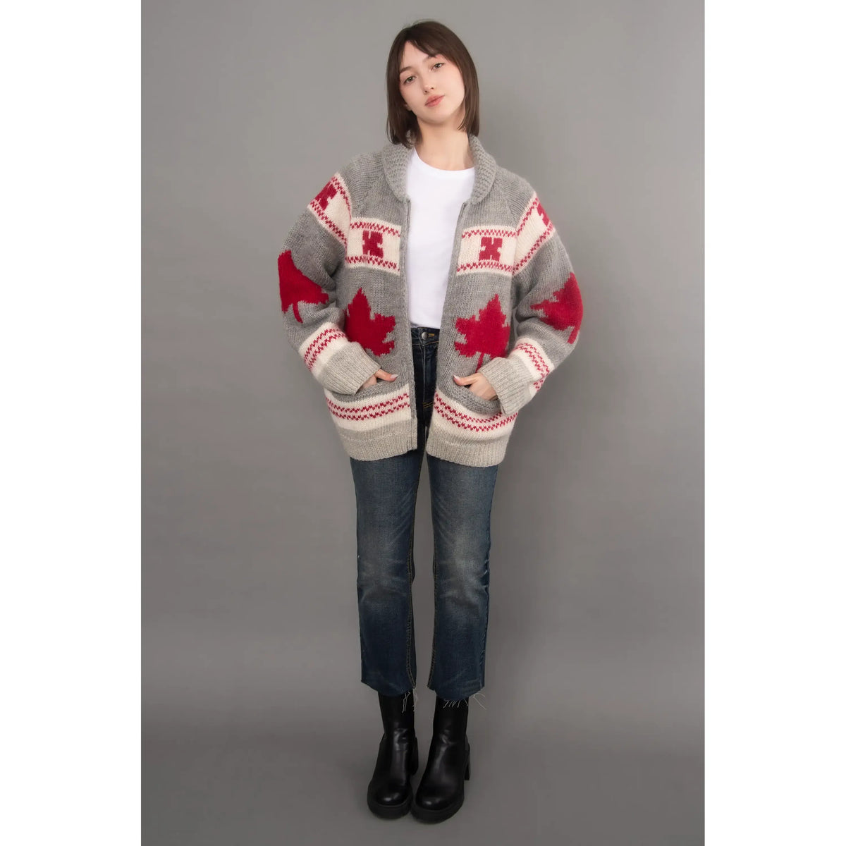 Gray knit cardigan with red maple leaf pattern, shawl collar, and raglan sleeves styled with blue jeans and black boots.