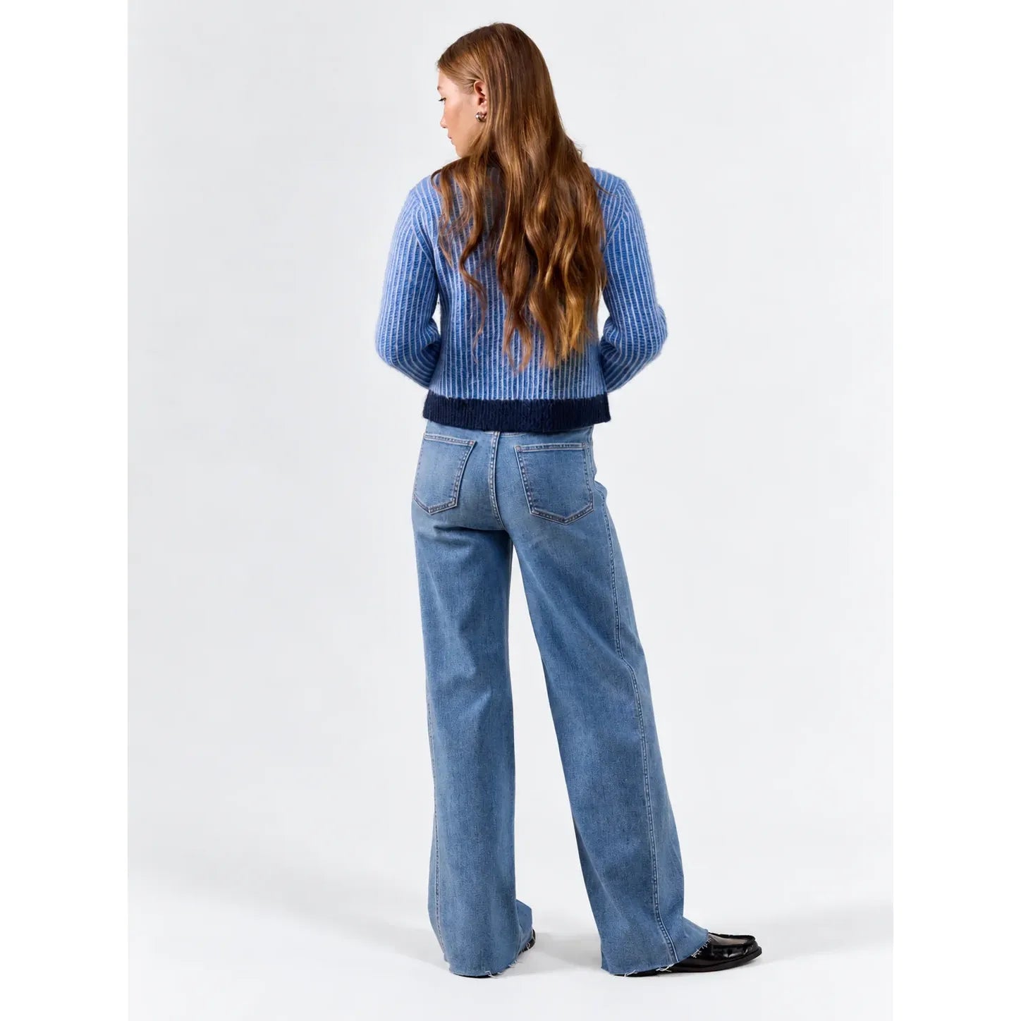 Back view of Daze Far Out wide leg jeans in medium wash. High-rise fit features vertical paneled seams and a raw hem paired with a blue sweater.