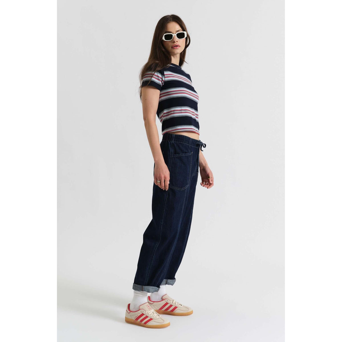 Model wearing Daze Villa Drawstring Barrel in Blue Mood pants with a striped crop tee, sunglasses, and sneakers.
