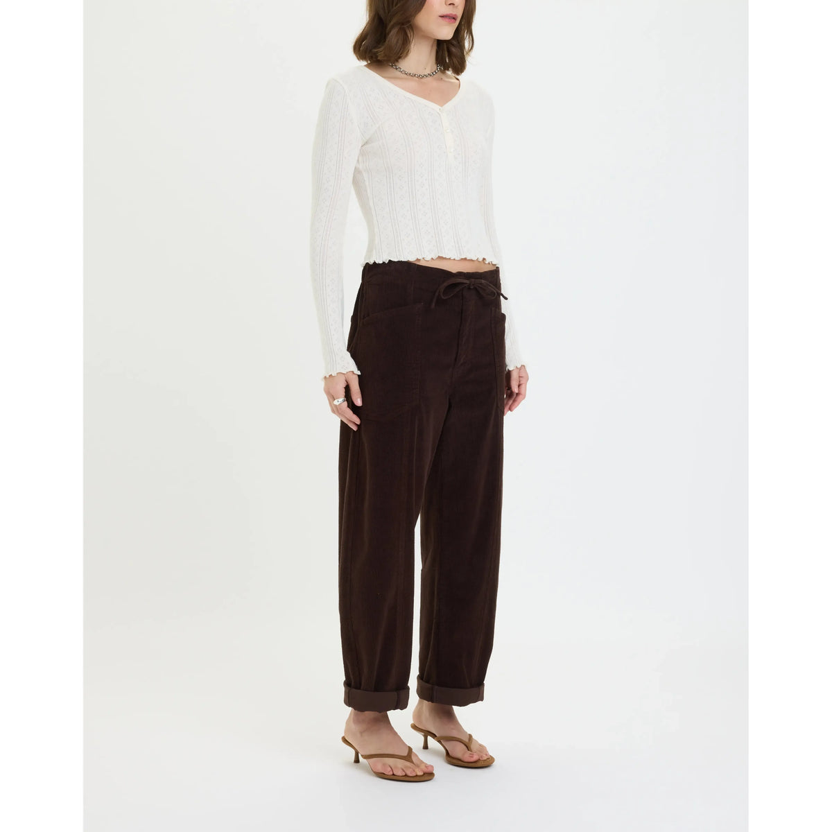 Model wears chocolate brown corduroy drawstring barrel pants with side pockets and cuffed ankles, styled with a white cropped top.