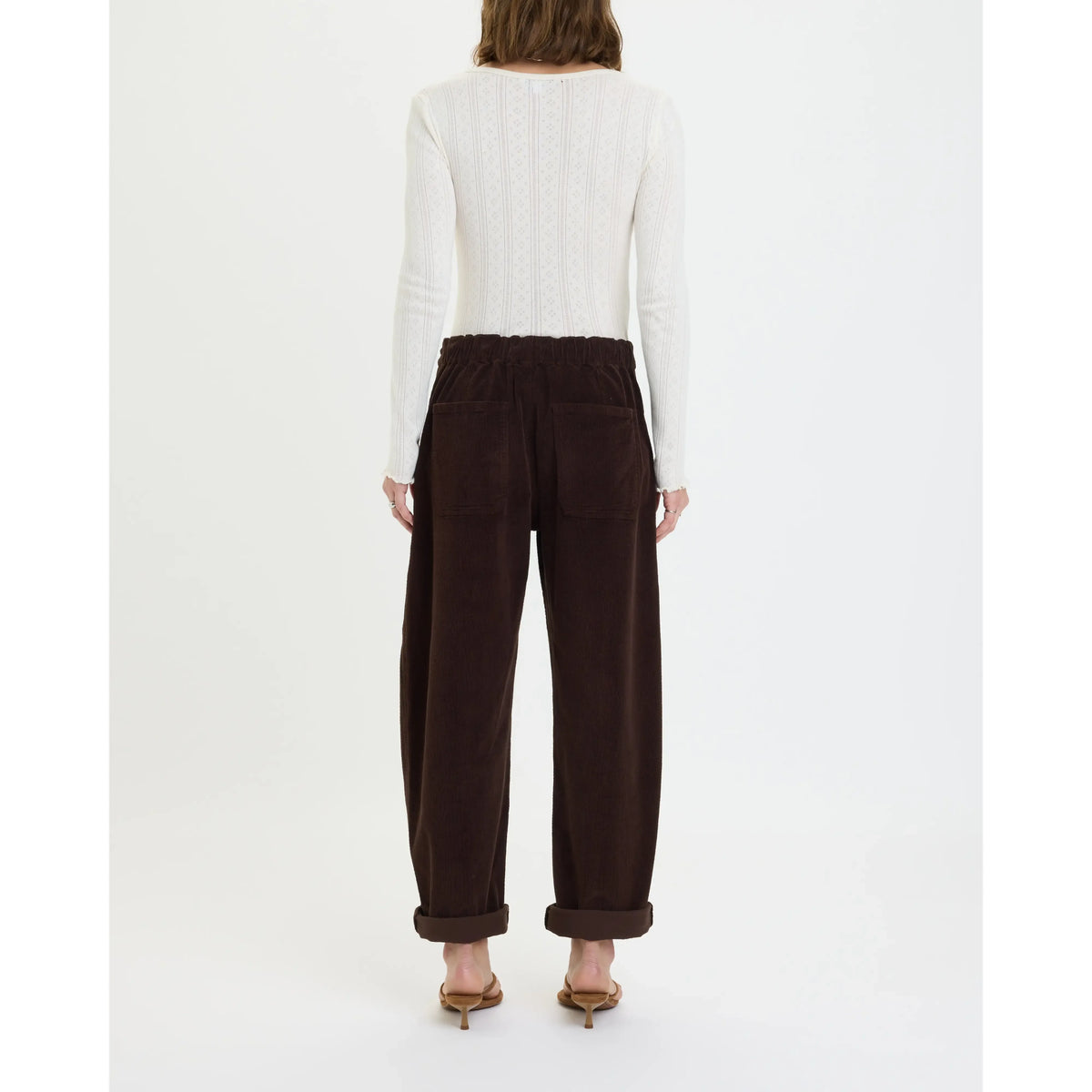 Back view of chocolate brown corduroy barrel pants featuring an elastic waist, rear patch pockets, and rolled cuffs for laid-back comfort.