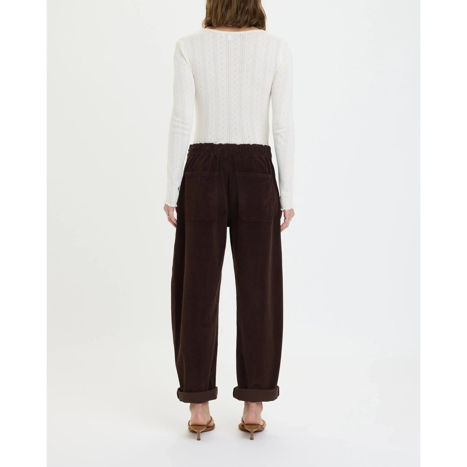 Back view of chocolate brown corduroy barrel pants featuring an elastic waist, rear patch pockets, and rolled cuffs for laid-back comfort.