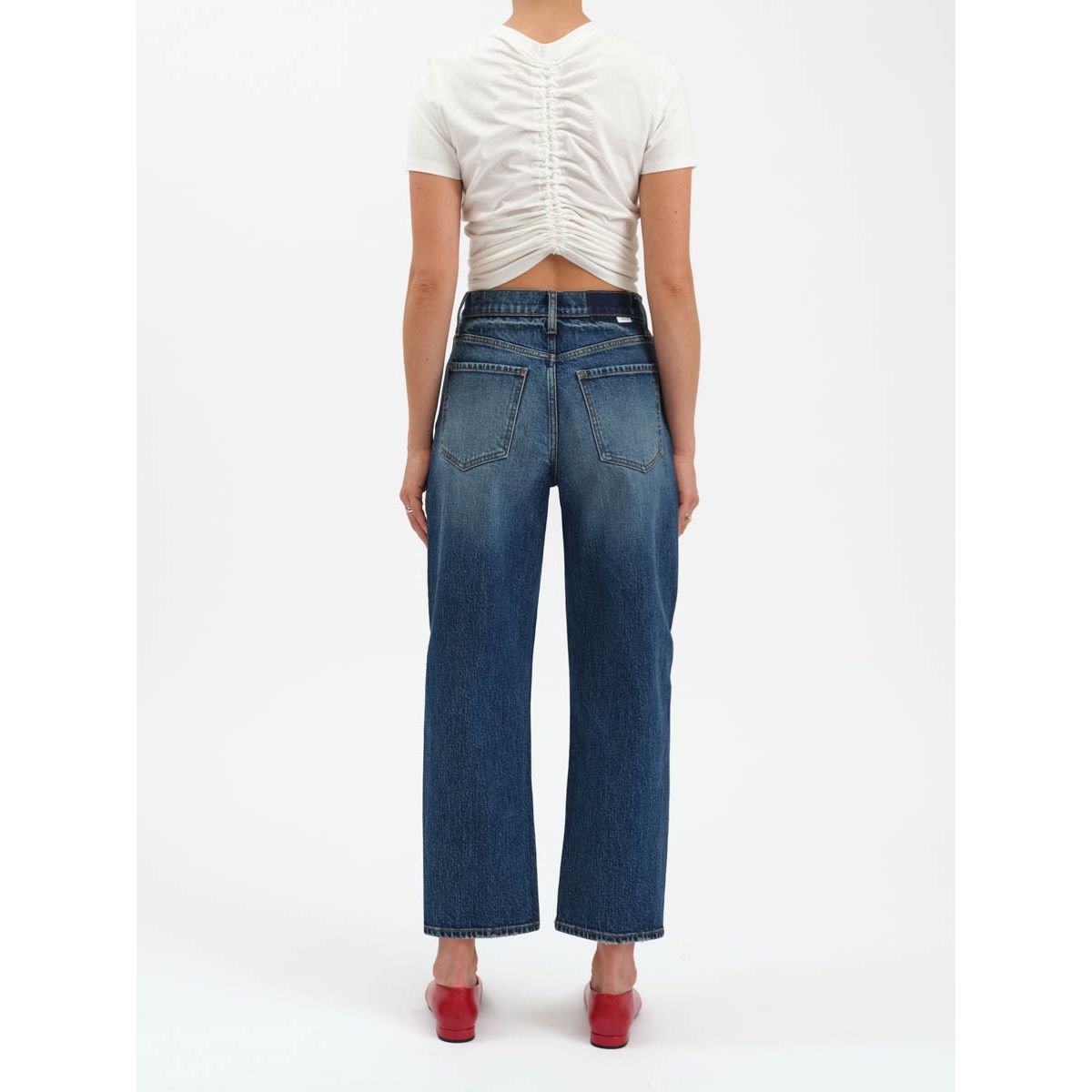 High-rise barrel-leg dark indigo jeans with a cinched waist and tapered ankle, styled with a white tee and red heels.