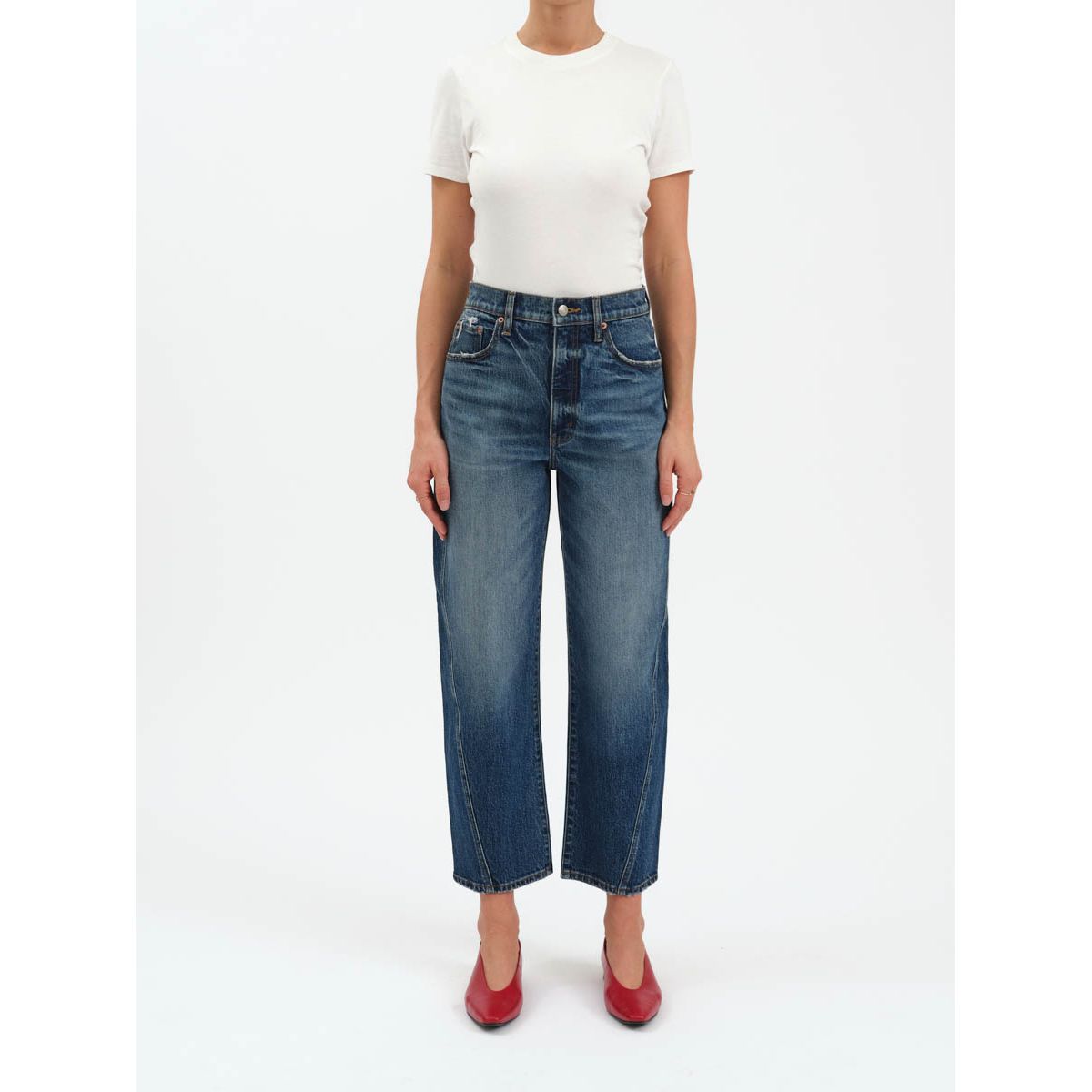 High-rise barrel-leg dark indigo jeans with a cinched waist and tapered ankle, styled with a white tee and red heels.