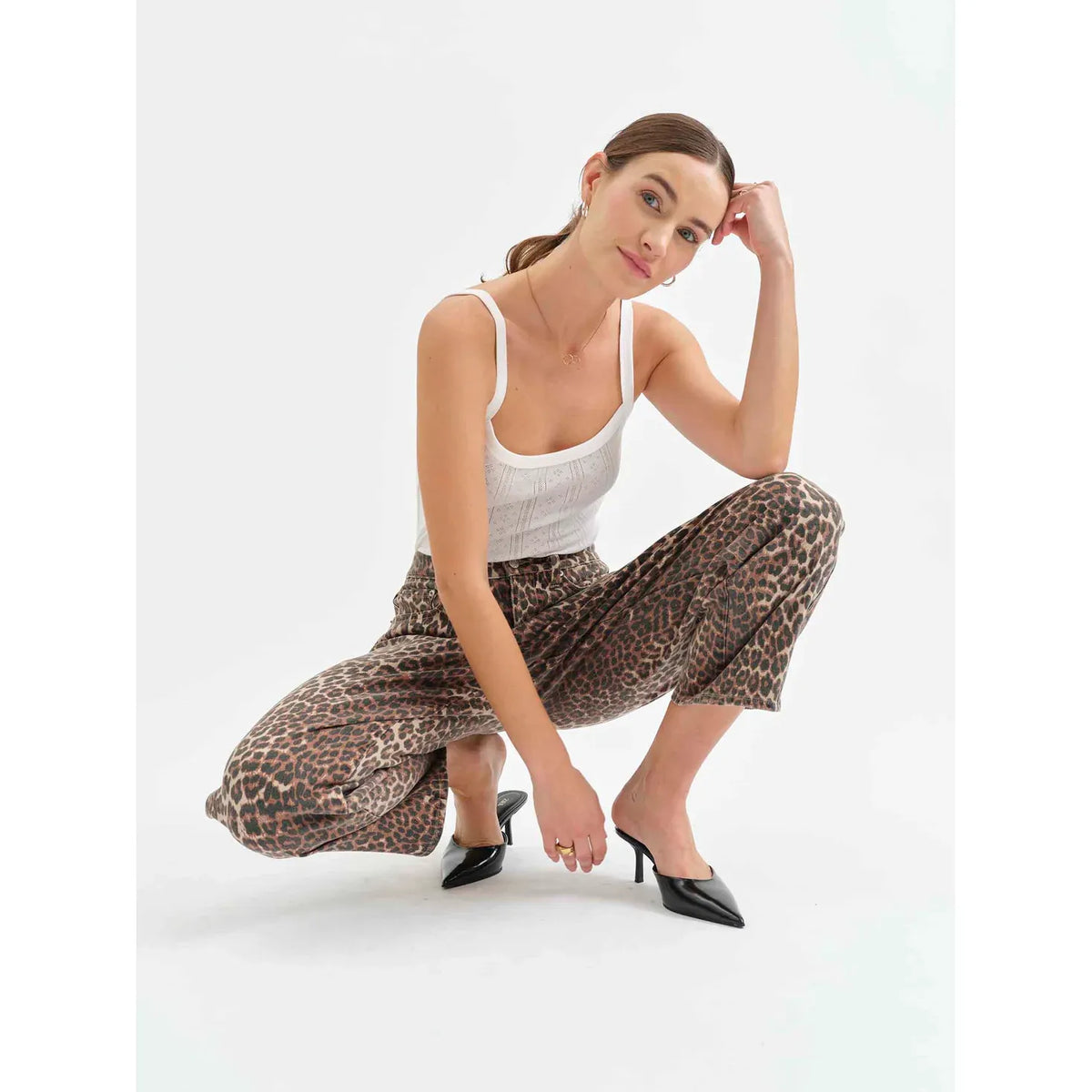 Model wearing Daze Westward Barrel Leg in Cool Cat leopard-print pants with white tank and black heels.