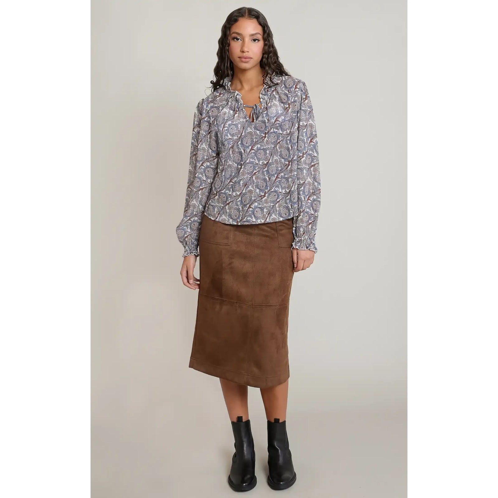 Woman wearing a patterned Dex balloon sleeved blouse with a V-neckline, paired with a brown midi skirt and black ankle boots.