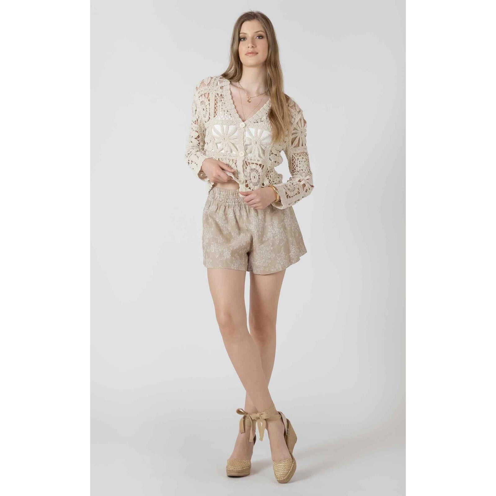 Cream crochet cardigan with embroidered square motifs and buttons, paired with beige shorts and tied-espadrille wedges.