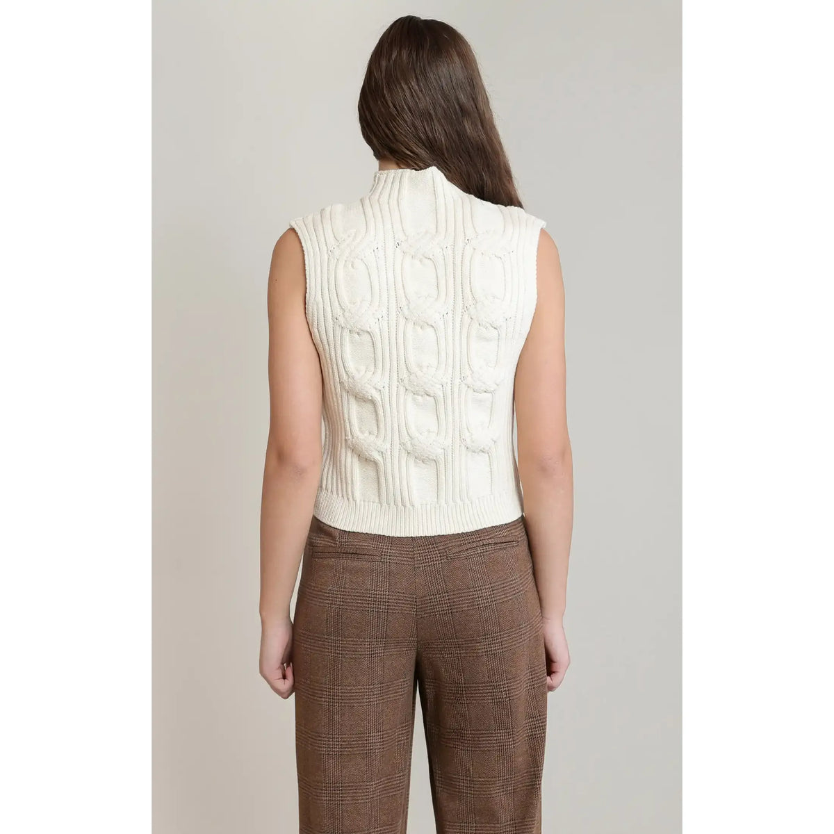 Back view of white cable knit sweater vest featuring textured weave and mock neck, paired with brown plaid trousers for fall layering.