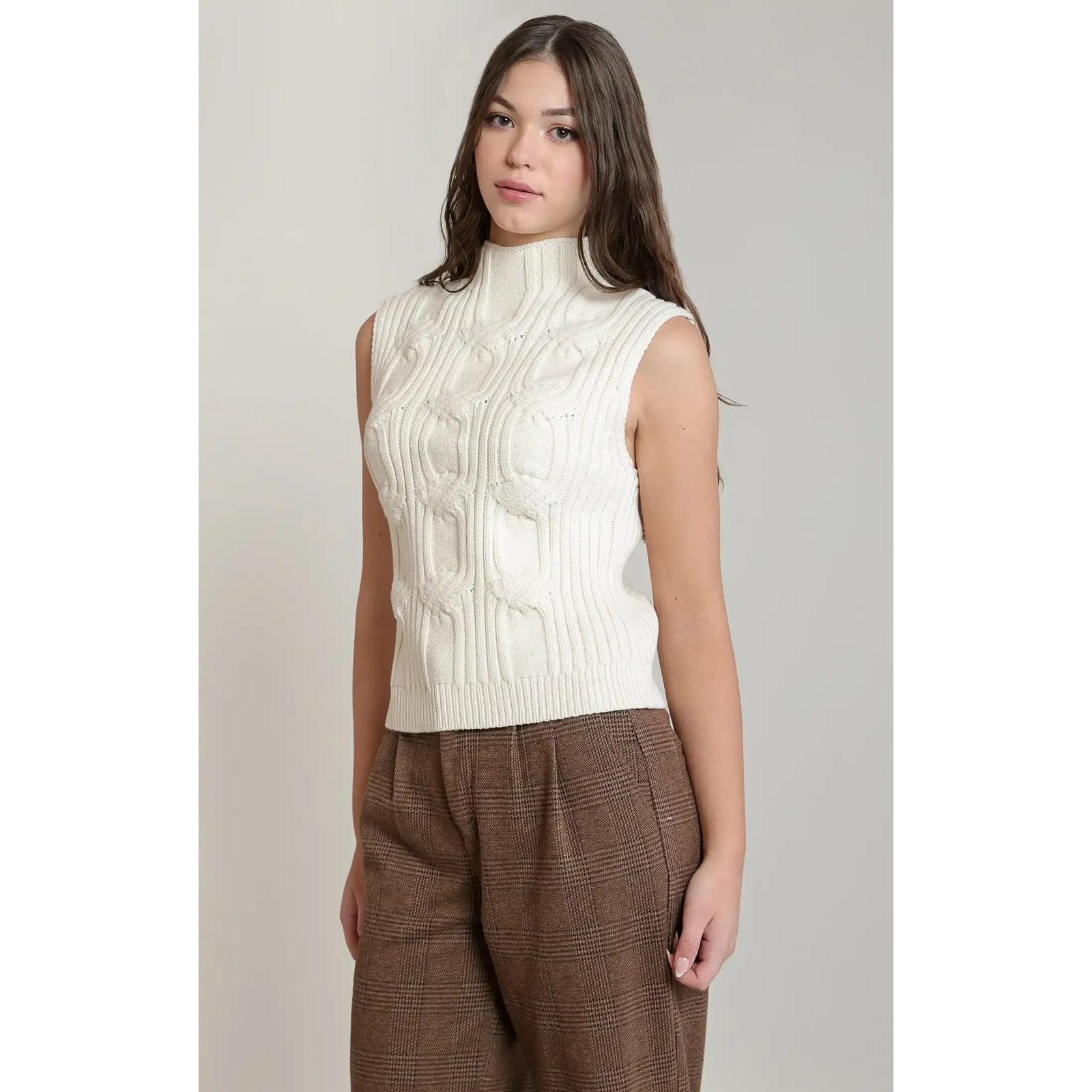 White cable knit sweater vest with a mock neck, paired with brown plaid trousers for fall styling.