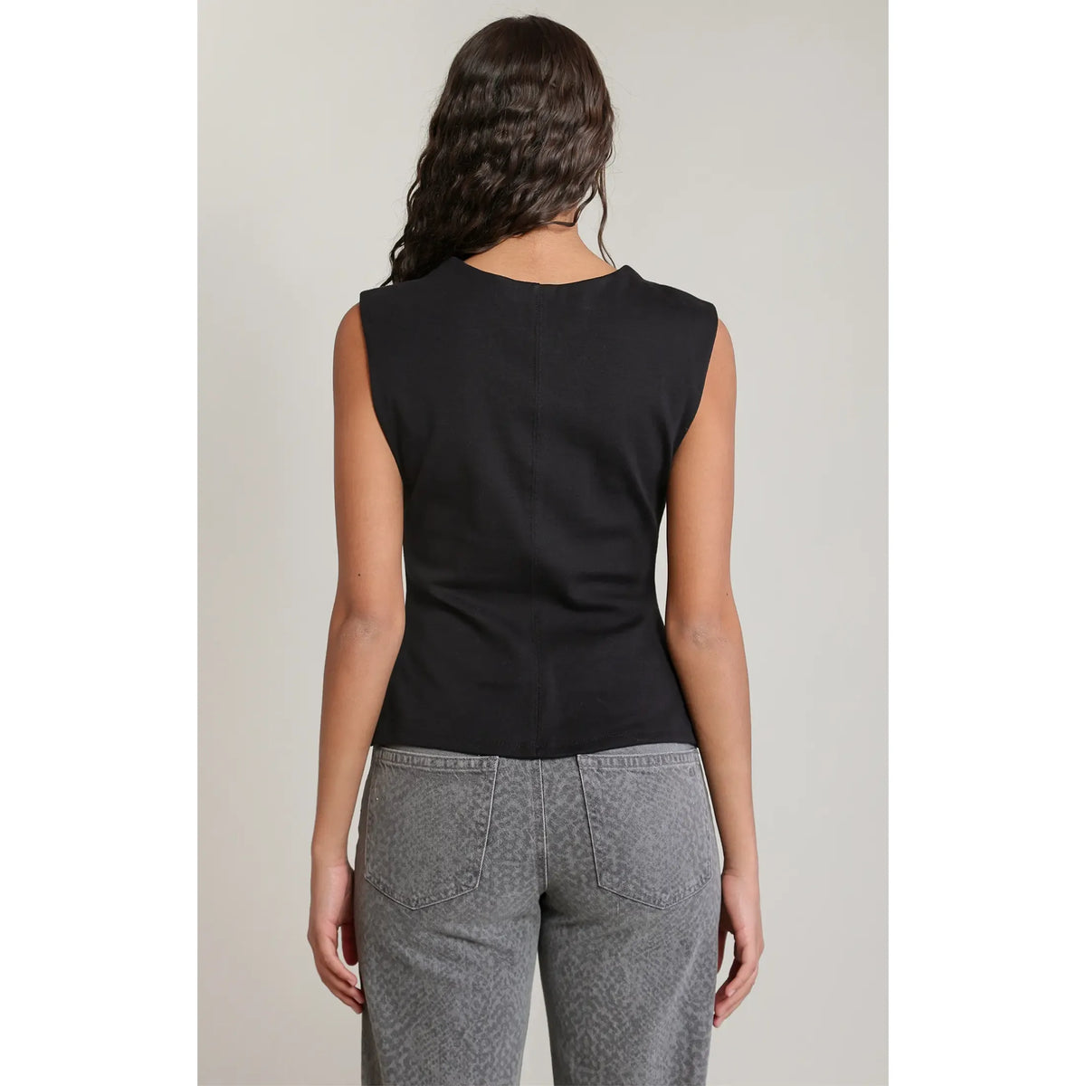 Back view of a black cinch waist sleeveless top featuring a center seam, paired with grey acid-wash jeans.