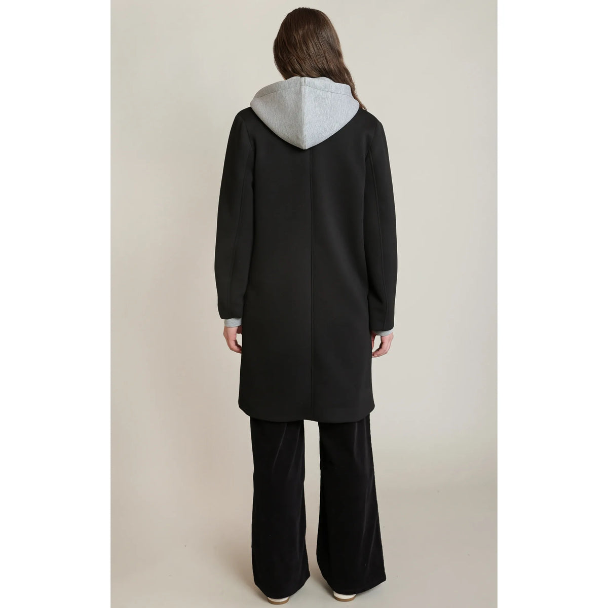 Back view of a black convertible hooded coat featuring a contrast grey attached hood and matching grey cuffs on a stretch-blend fabric.