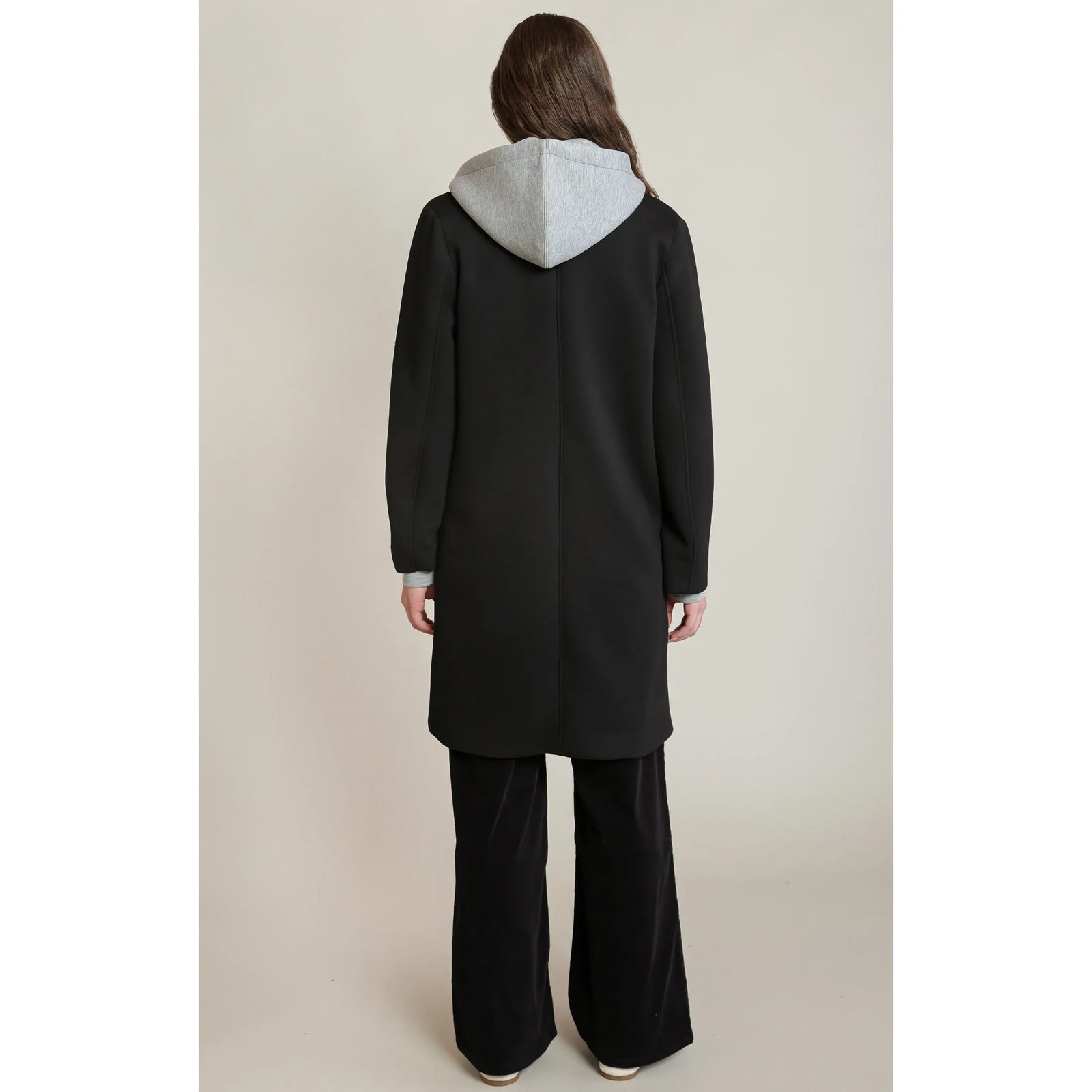 Back view of a black convertible hooded coat featuring a contrast grey attached hood and matching grey cuffs on a stretch-blend fabric.