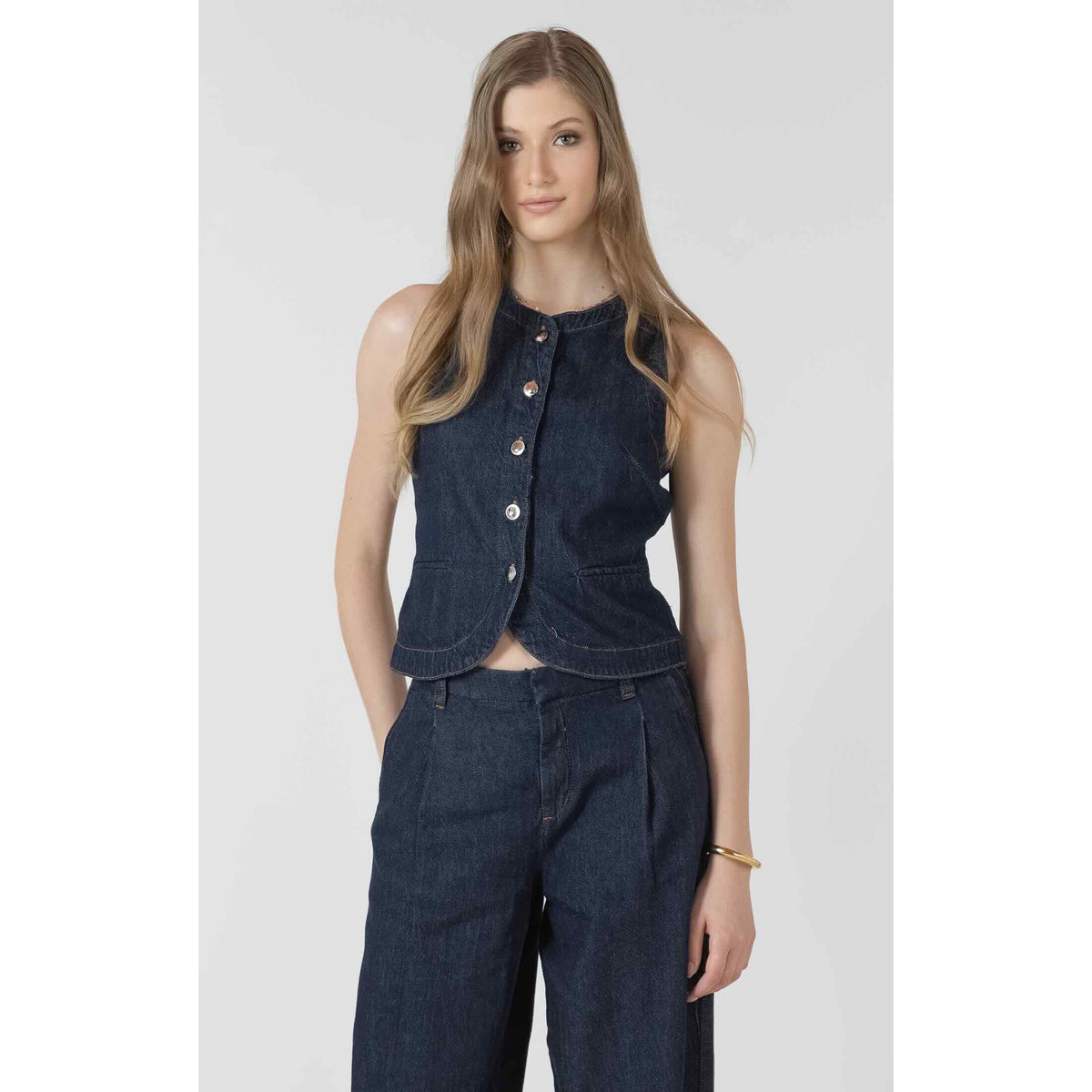 Dex Black Tape Denim Vest on a model, dark indigo sleeveless button-up denim top with curved hem.