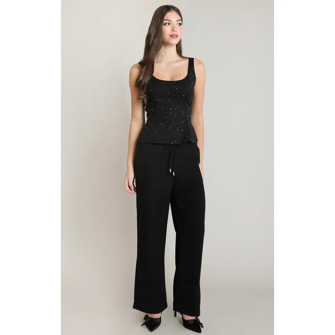 Black sleeveless peplum top with sparkling embellishments, flared waist silhouette, paired with black wide-leg trousers and heels.