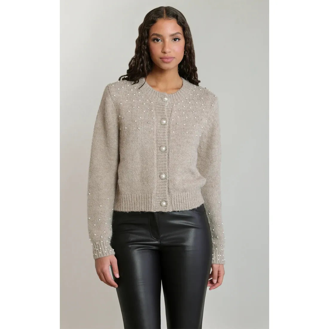 Beige embellished crewneck cardigan with scattered pearls, pearl buttons, and relaxed silhouette paired with black leather pants.