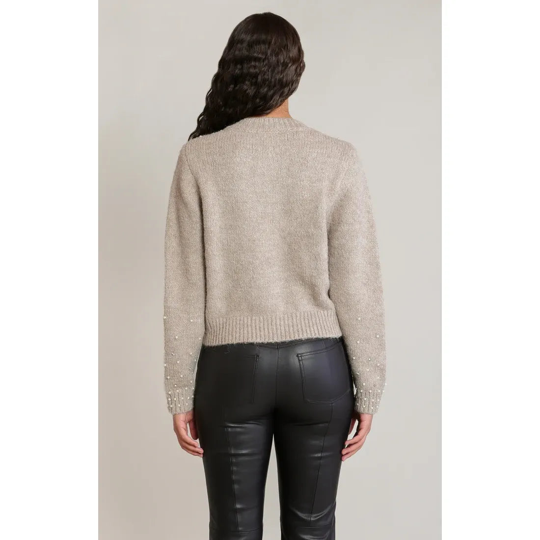 Back view of beige embellished crewneck cardigan featuring pearl detailing on sleeves, paired with black leather pants.