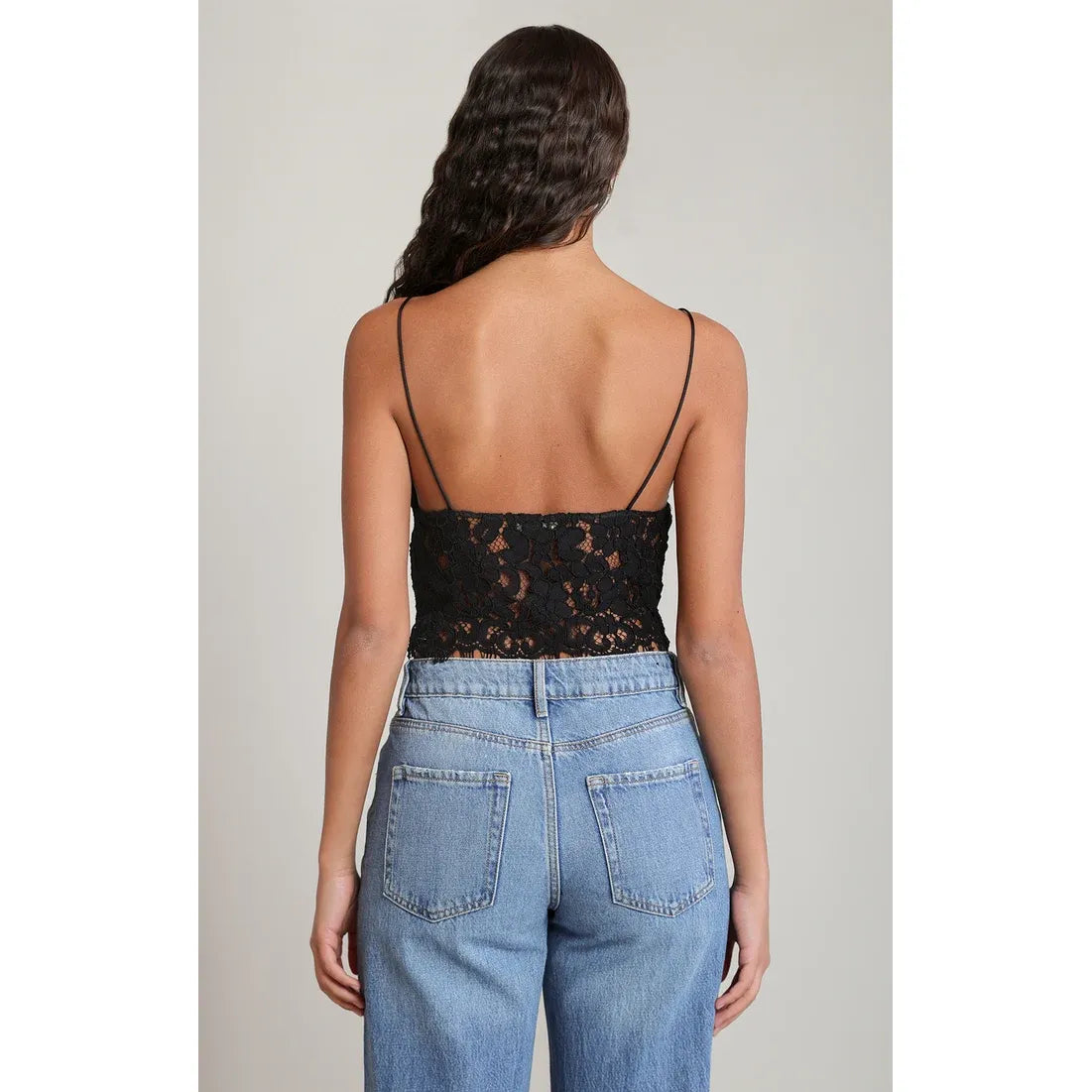 Back view of a black embroidered camisole top with thin straps, paired with blue denim jeans.