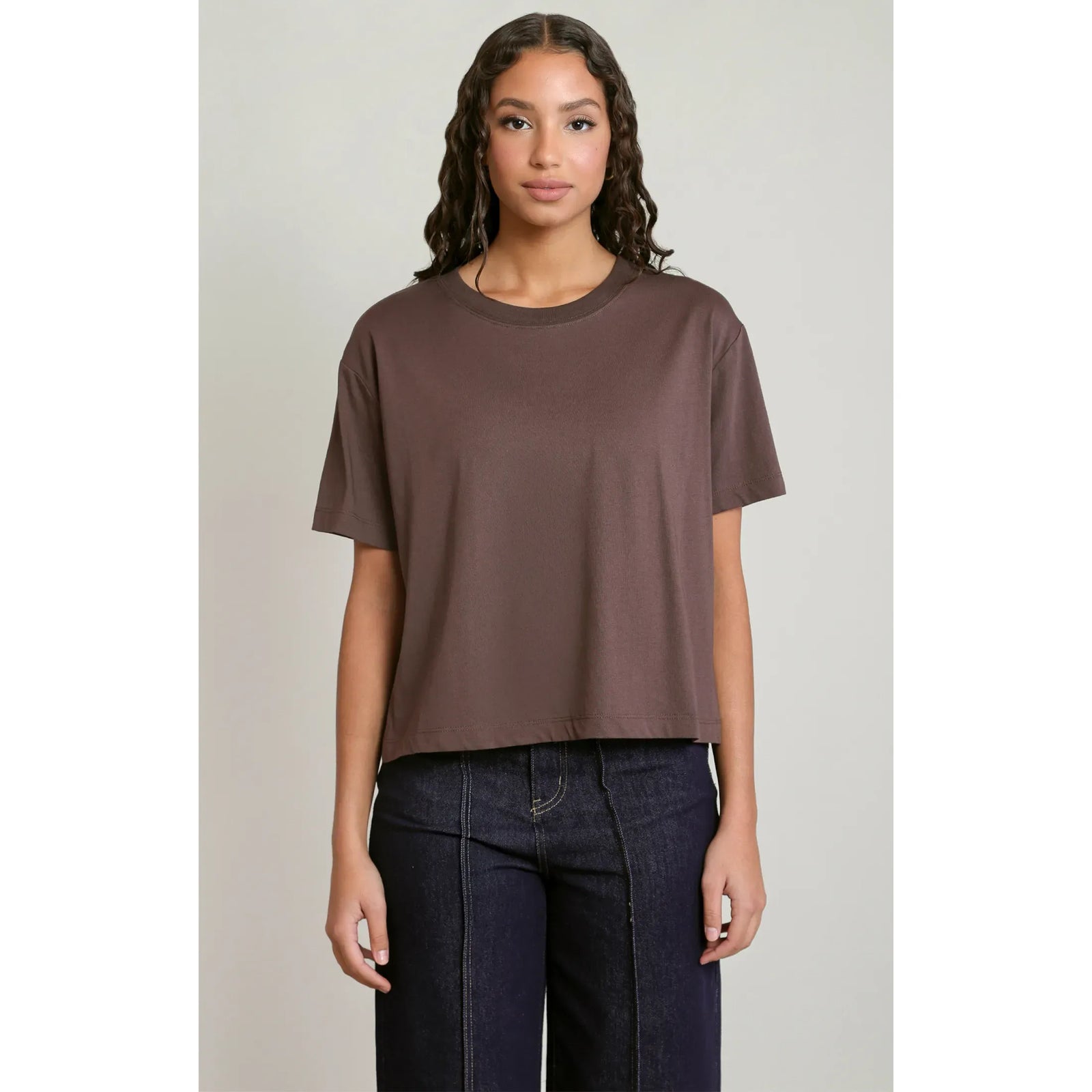 Brown short-sleeved essential tee with a relaxed fit and round neck, styled here with dark denim jeans.