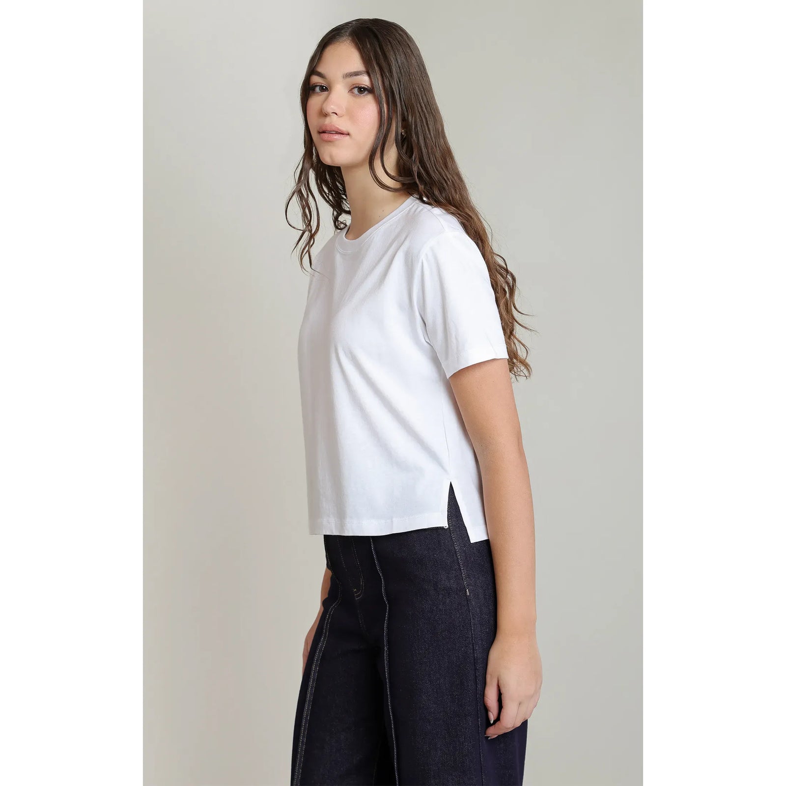 Woman wearing a white short-sleeved essential tee with a round neck and side slit hem, paired with dark denim jeans for a relaxed fit.