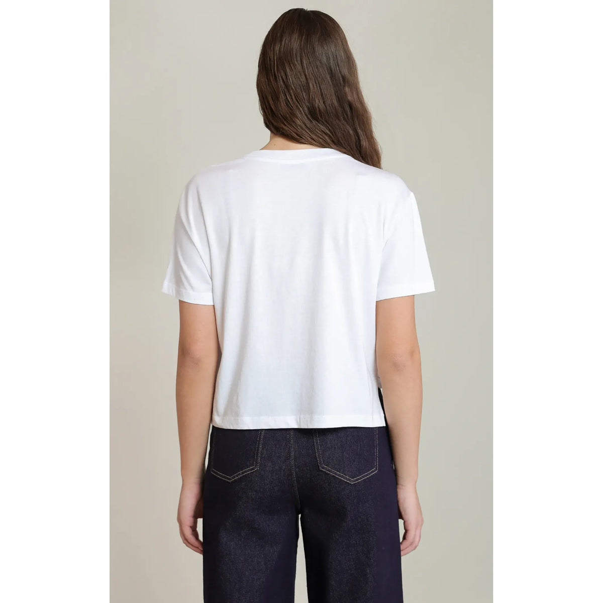 Back view of a white short-sleeved essential tee with a relaxed fit, paired with dark denim jeans for everyday comfort.