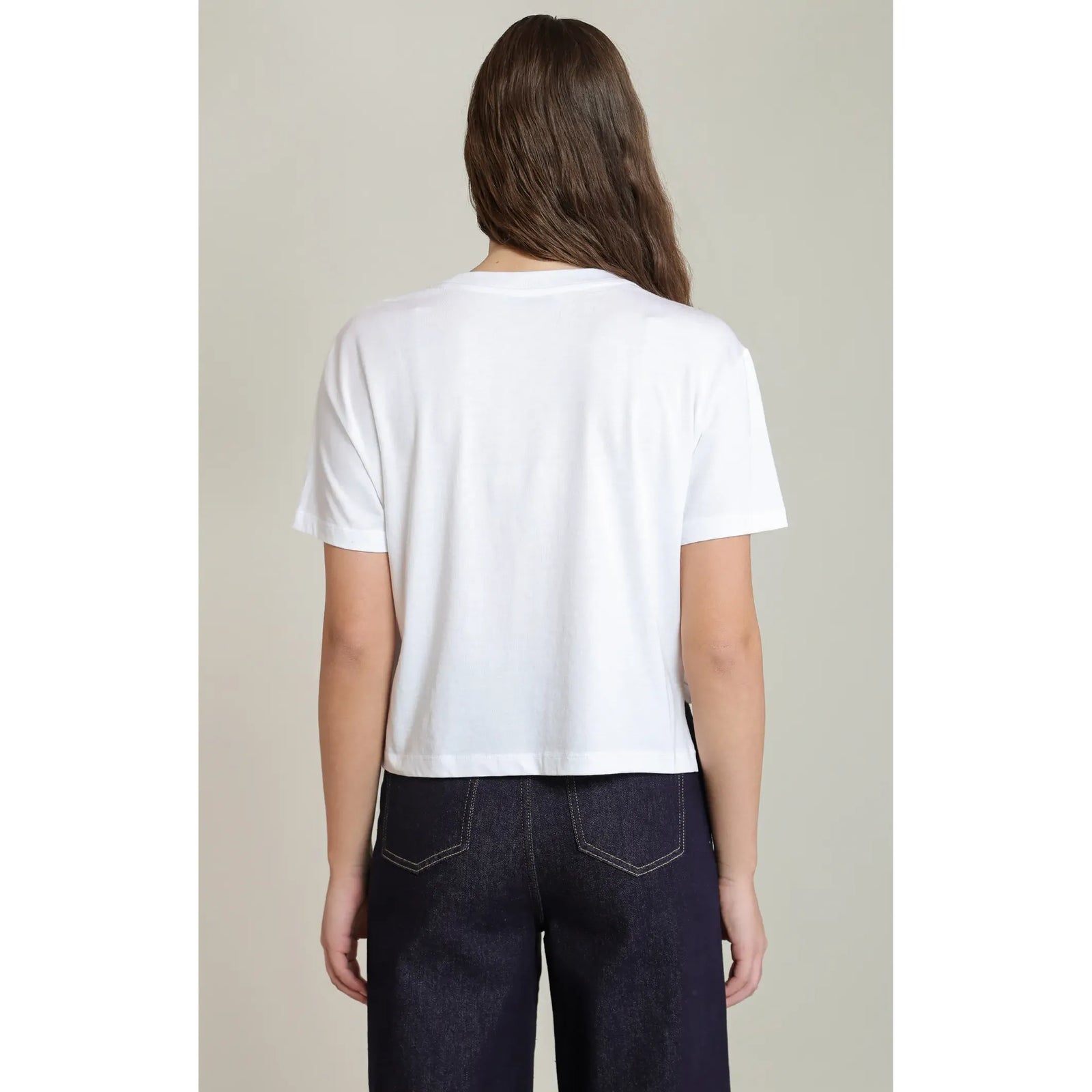 Back view of a white short-sleeved essential tee with a relaxed fit, paired with dark denim jeans for everyday comfort.