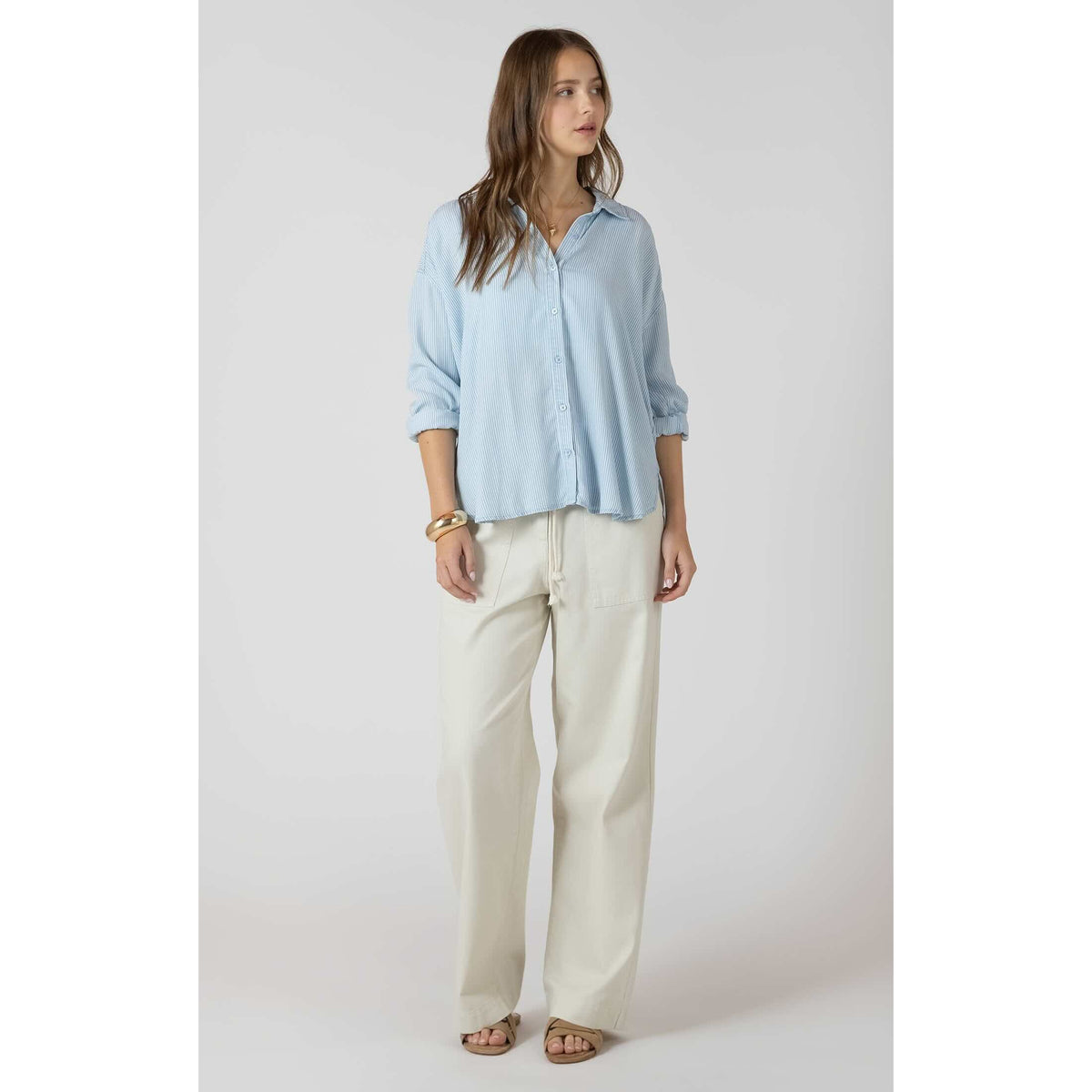 Dex Relaxed Button Front Shirt in light blue stripes, relaxed fit, rolled sleeves, paired with ivory pants.
