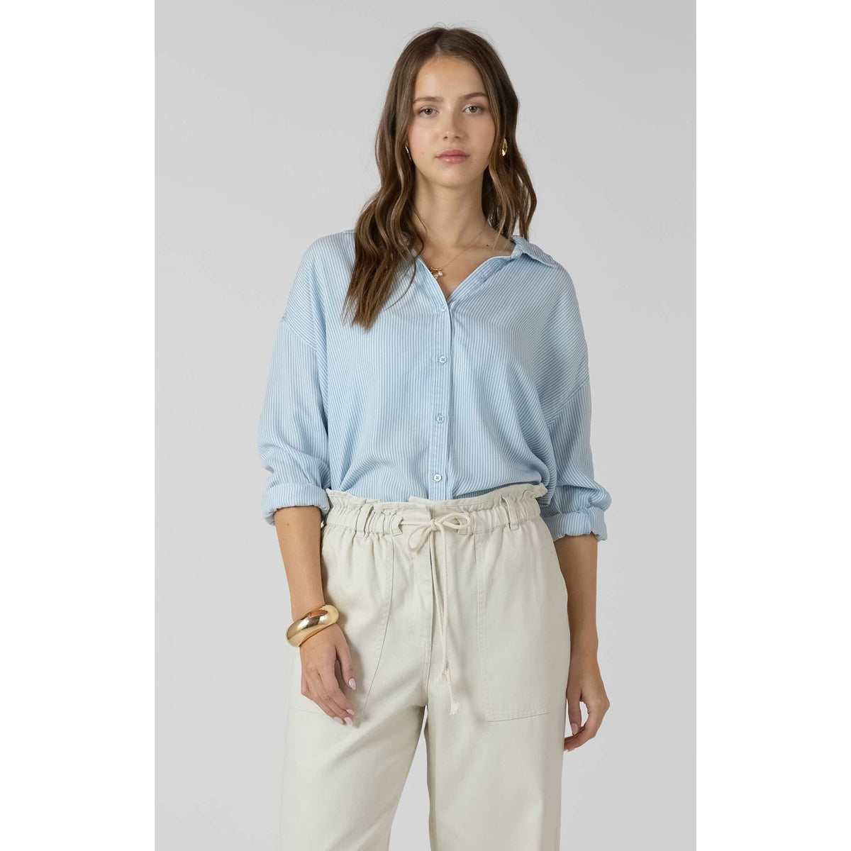 Model wearing a light blue striped Dex Relaxed Button Front Shirt with rolled sleeves and cream drawstring pants.