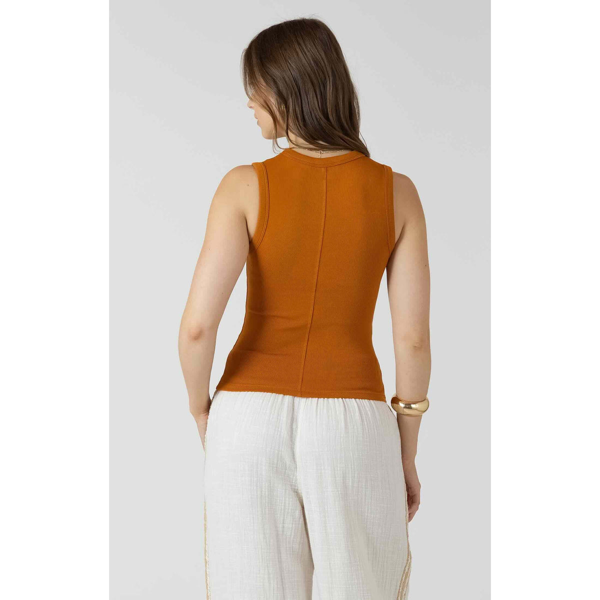 Dex Ribbed Tank in rust orange, ribbed fabric, back view on model with white linen pants.