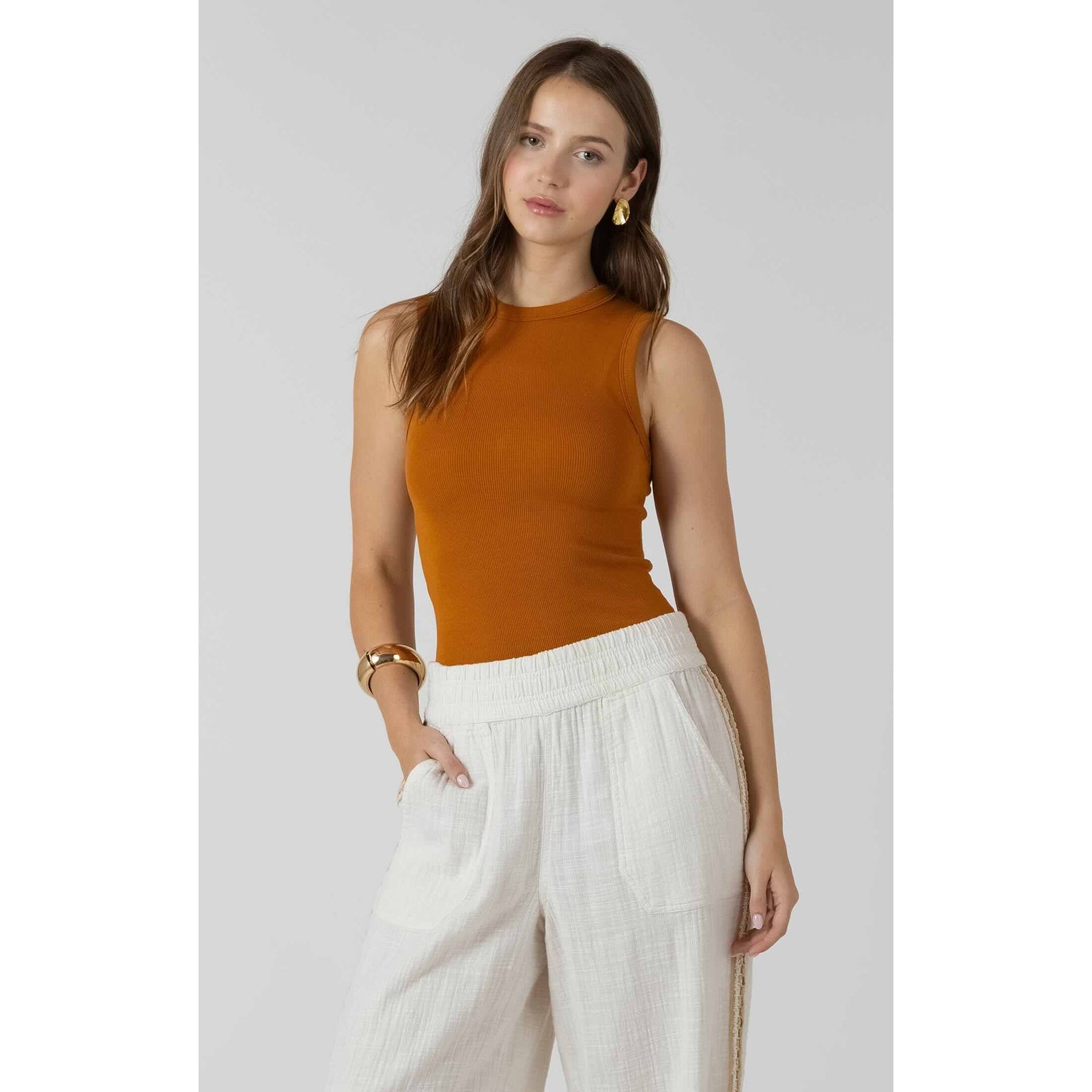 Dex Ribbed Tank in rust-orange ribbed fabric worn with white wide-leg pants.