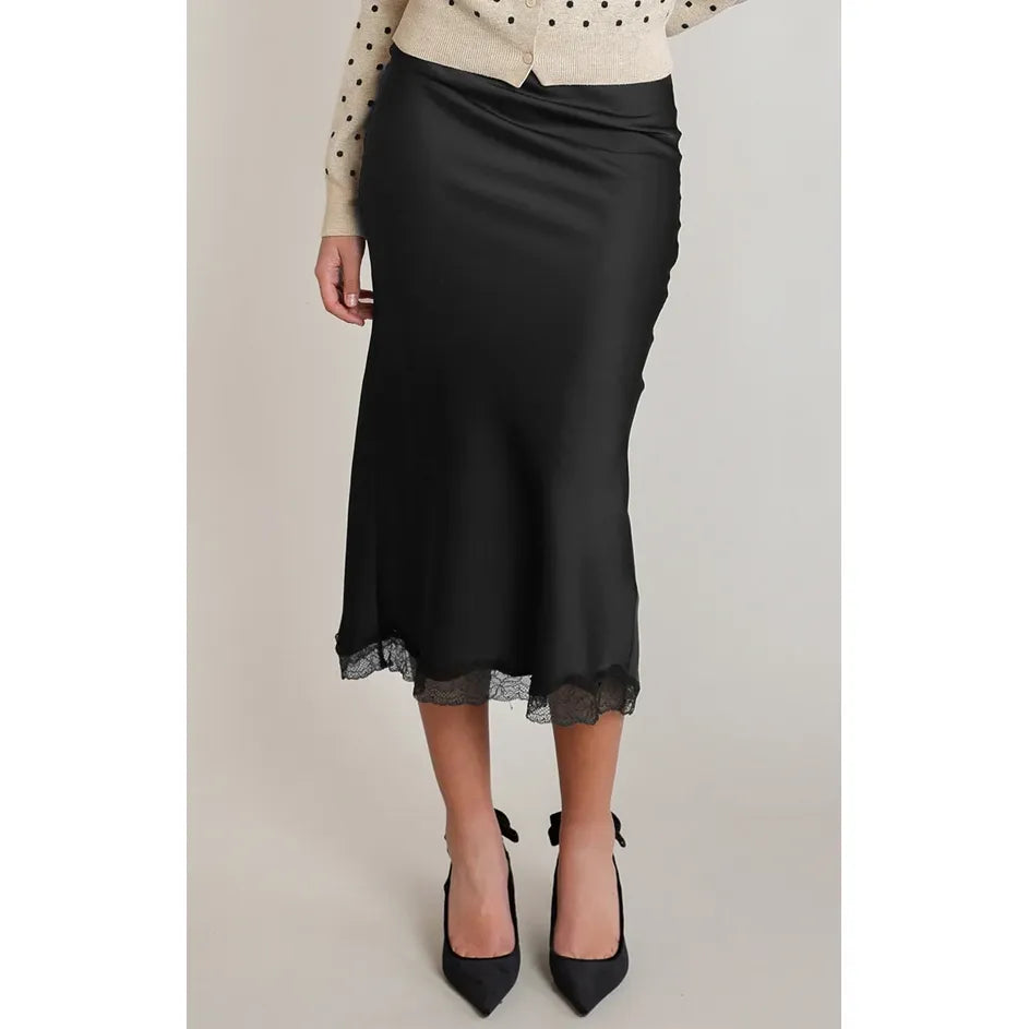 Black satin midi skirt with delicate lace hem, featuring a fluid drape and sophisticated silhouette paired with black heels.